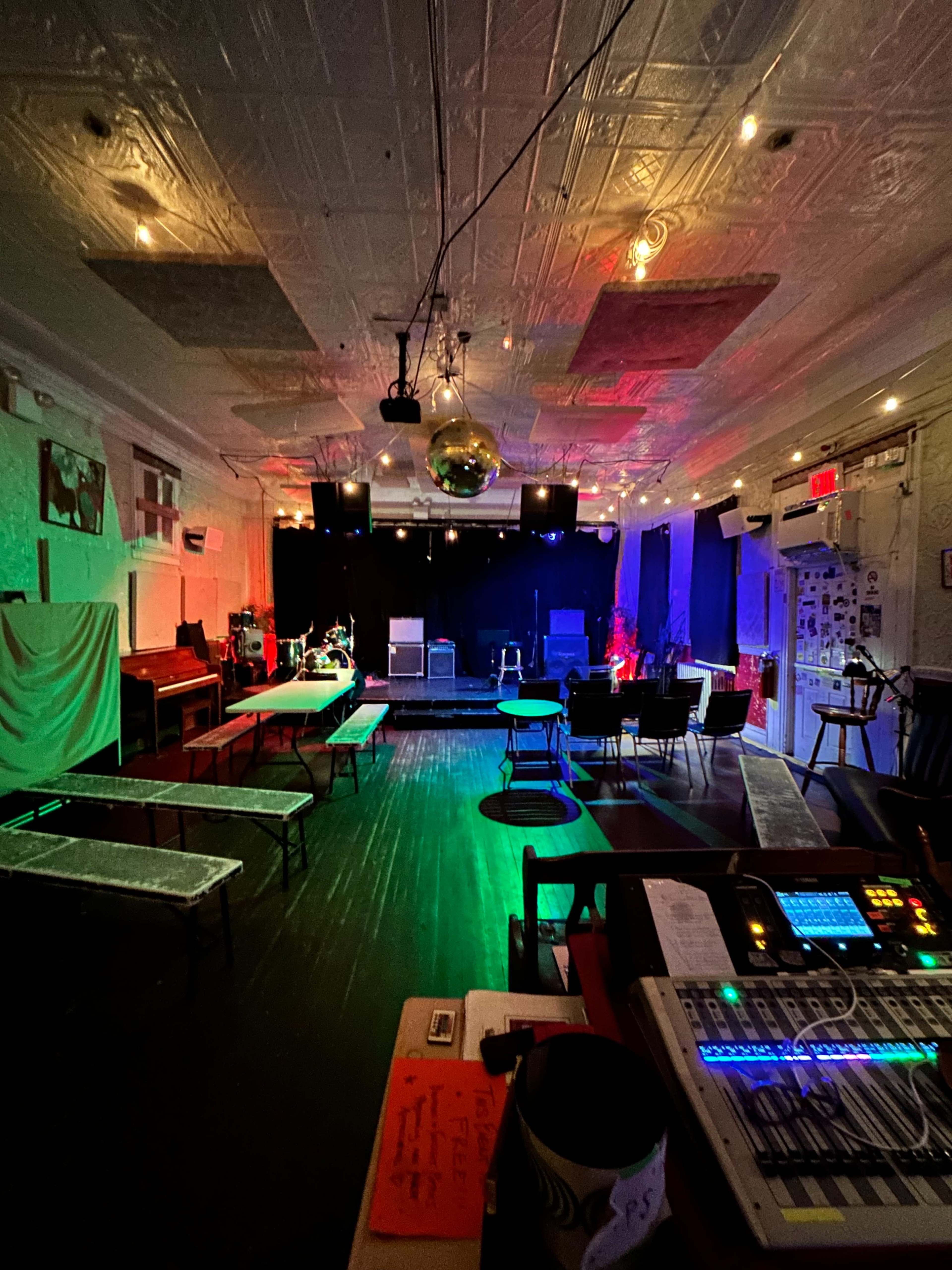 The image shows an empty performance venue with stage lighting, chairs, and equipment set up for a music event.