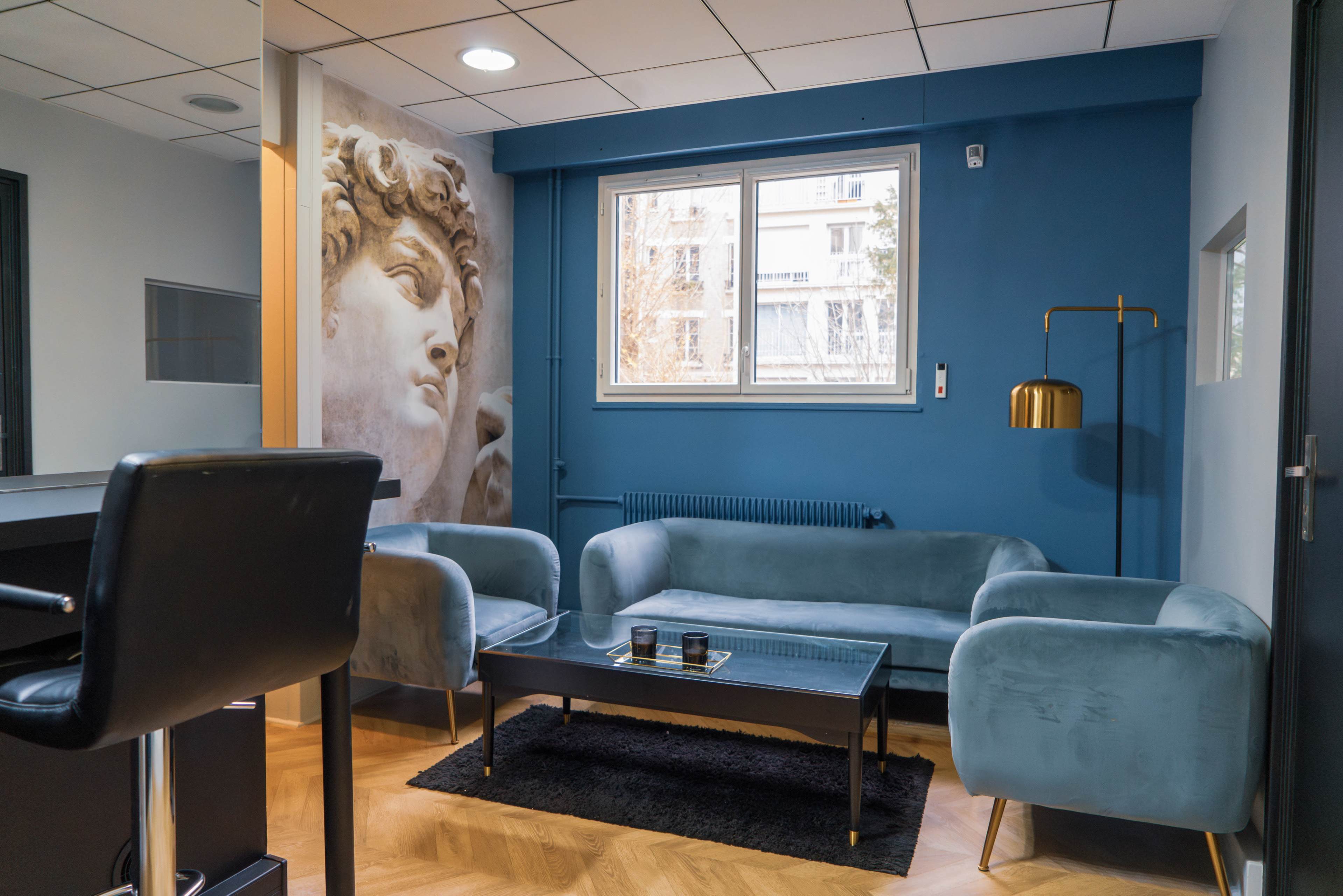 A modern sitting area with two light blue sofas, a black coffee table, and a large mural of a classical sculpture on the wall.