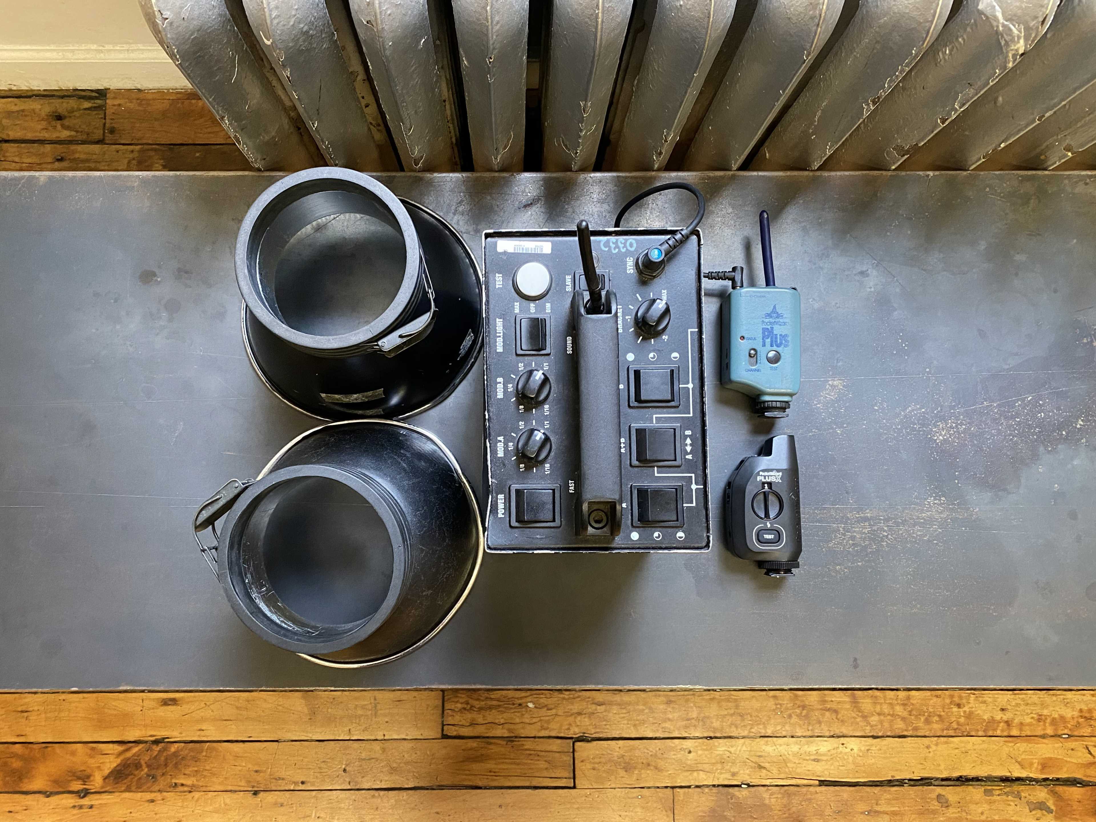 The image shows a tabletop with a mixing console, two black circular attachments, and a wireless remote control on a wooden floor.