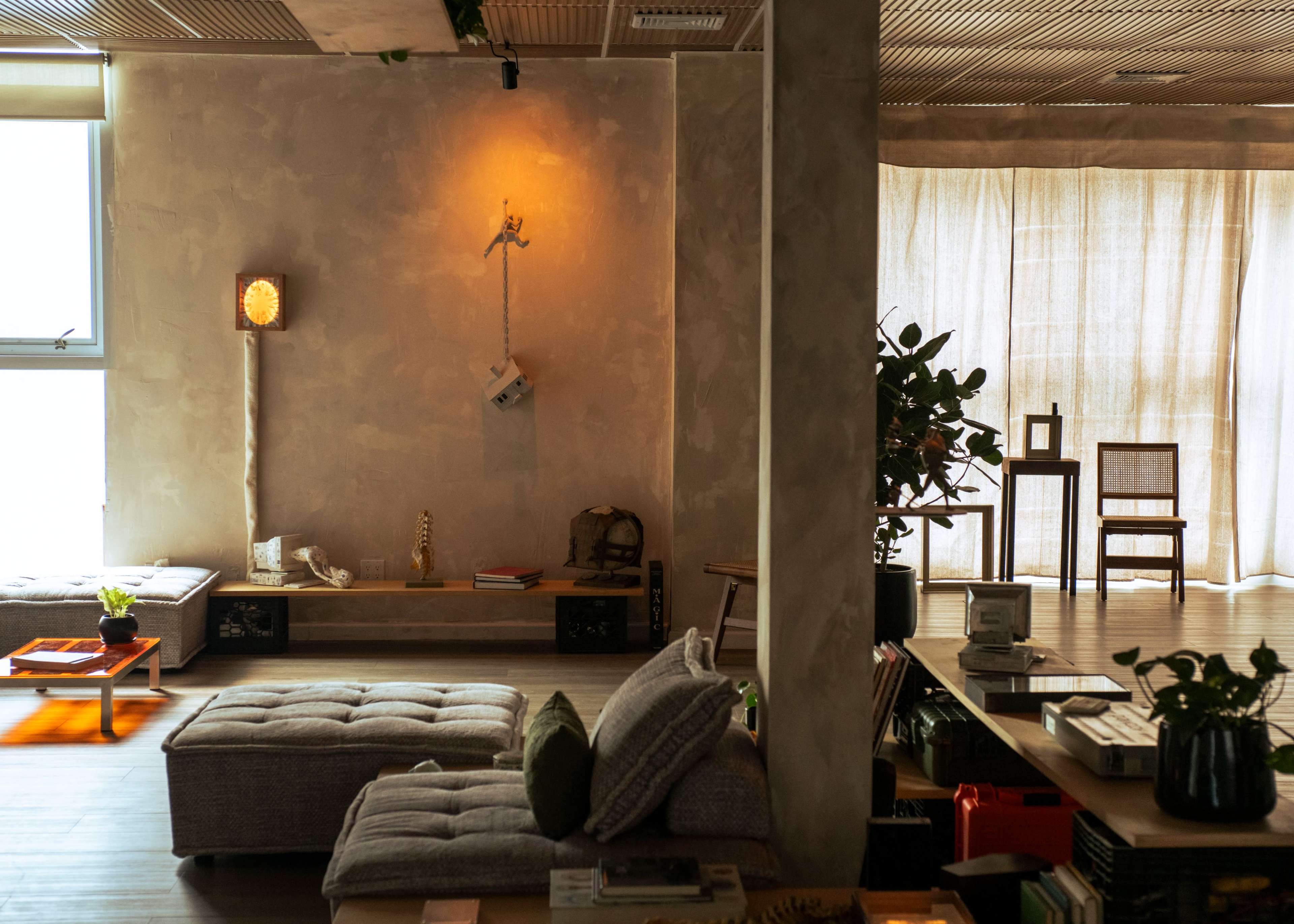 The image shows a modern interior space with a mix of seating areas, wooden furniture, and decorative plants.