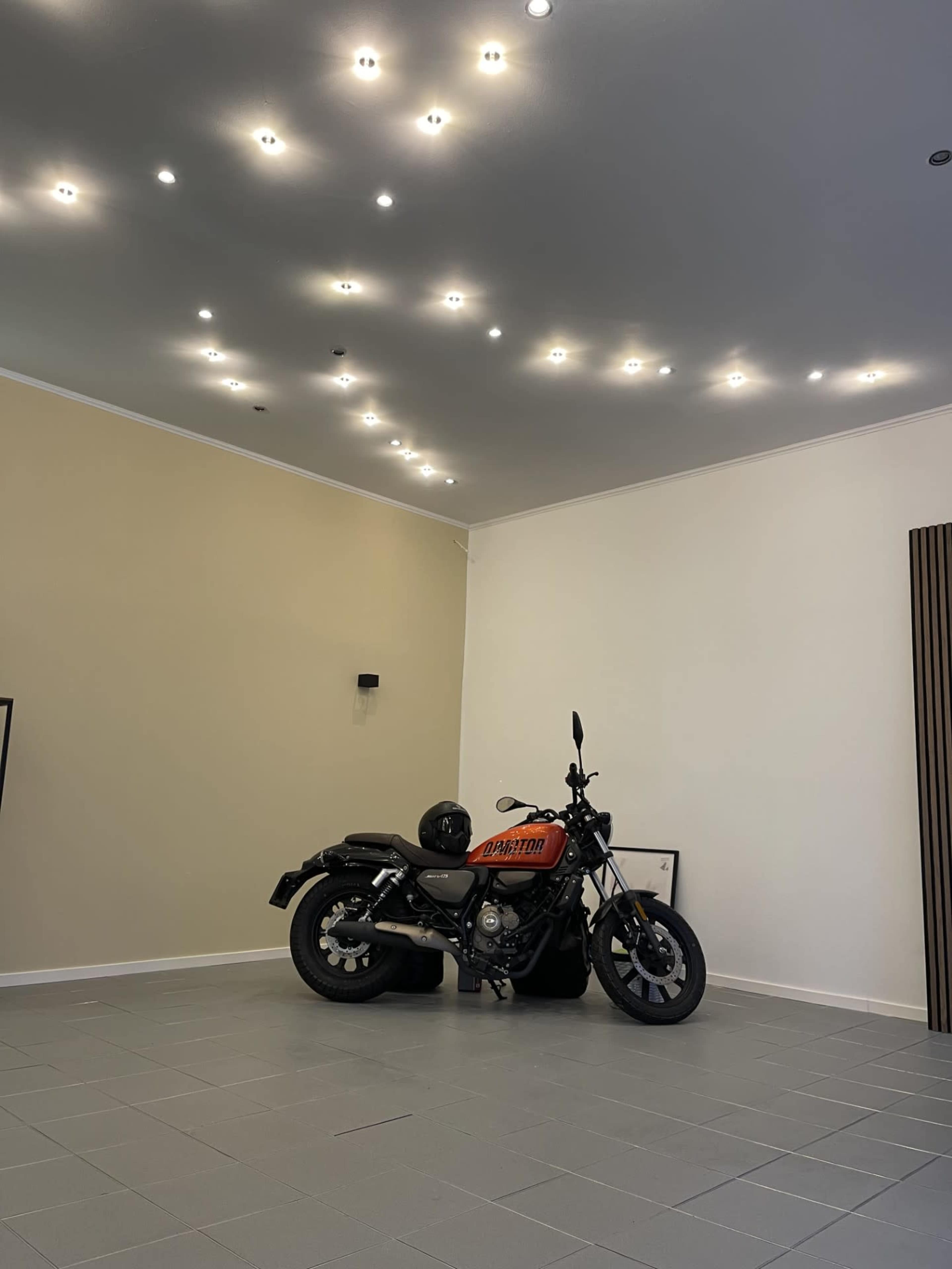 A motorcycle with an orange and black design is parked in a spacious room with white walls and modern lighting.