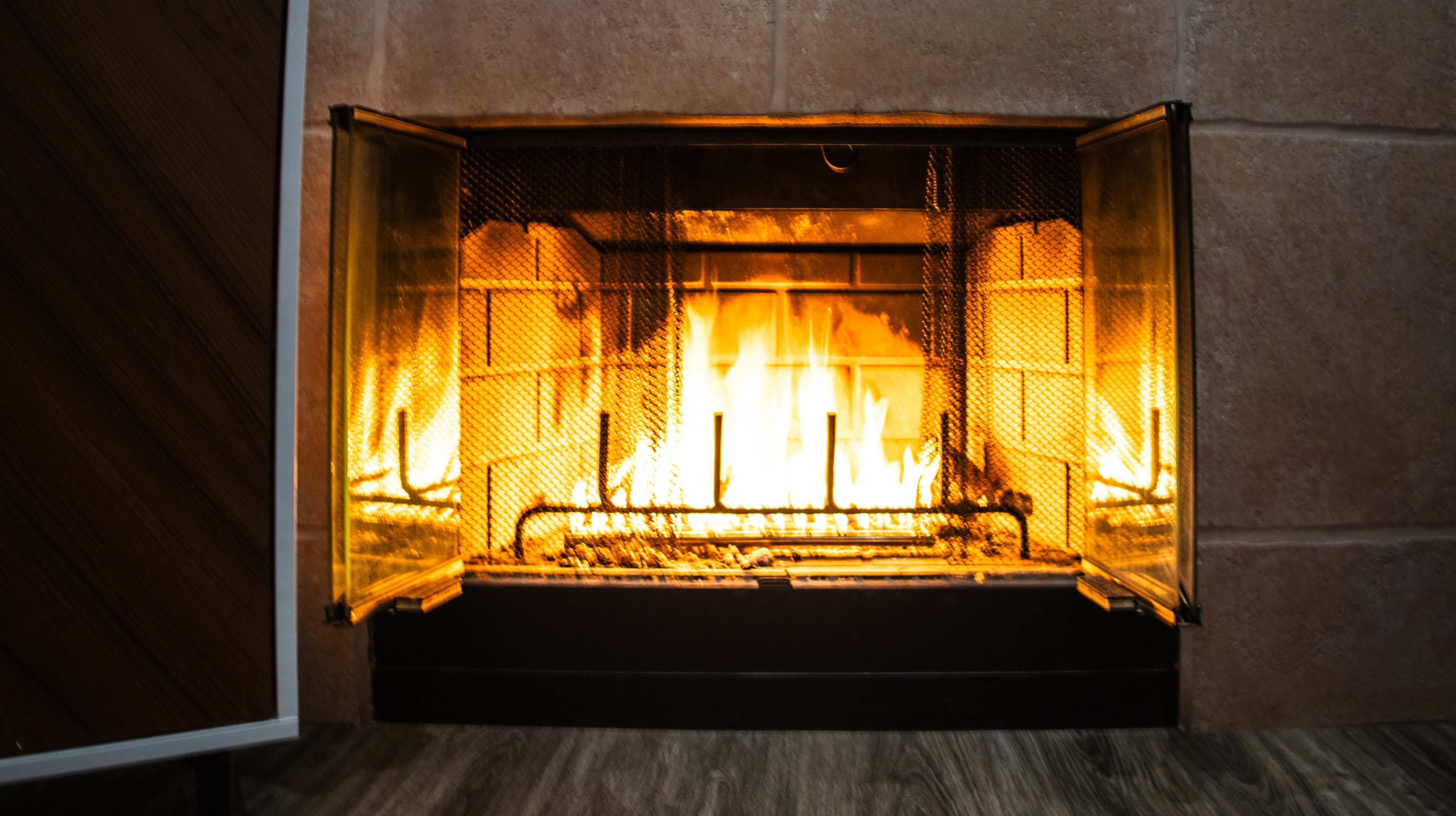 A fire burns brightly inside a glass-fronted fireplace with a stone and wood surround.