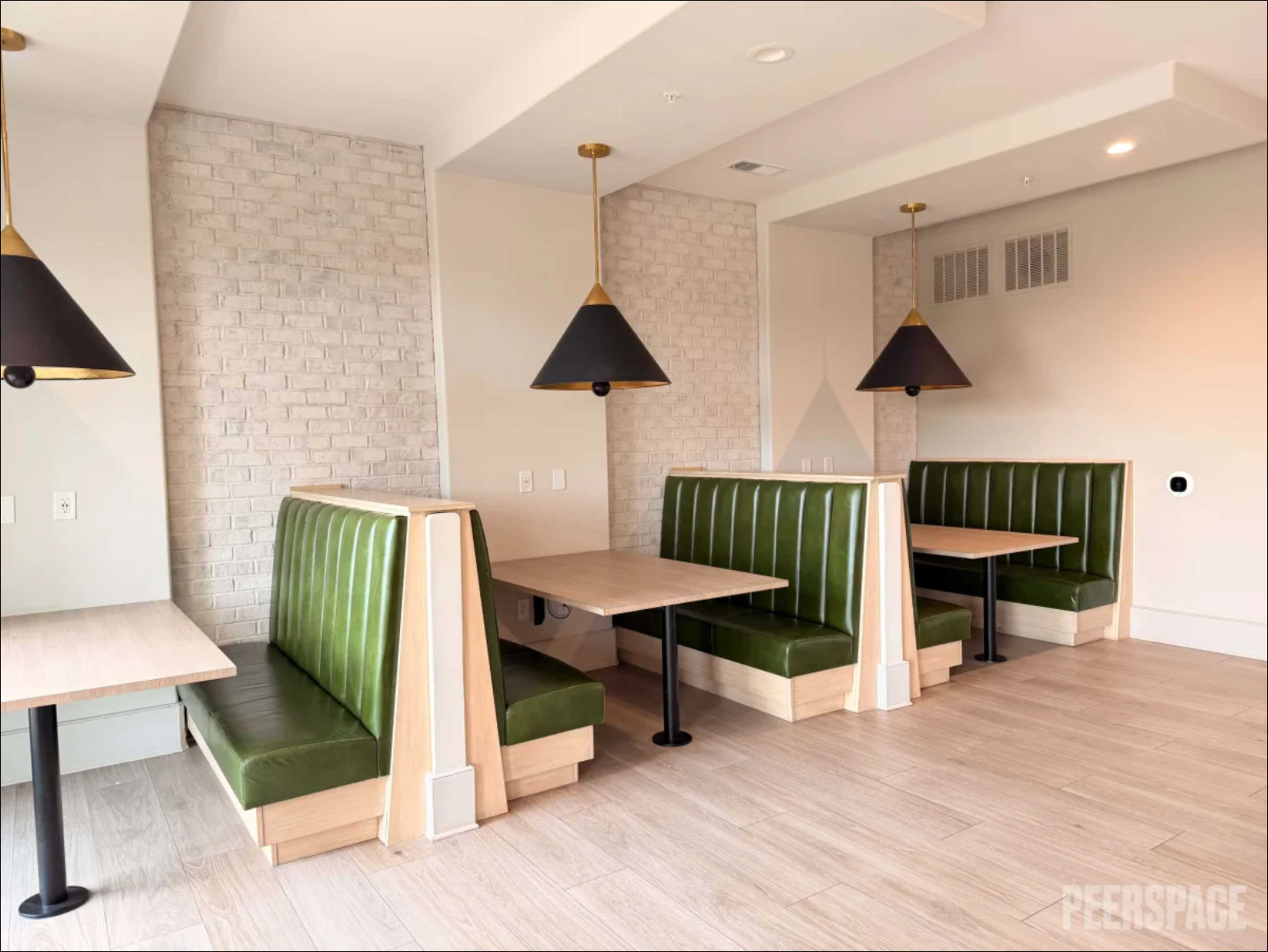 The image shows a modern restaurant interior featuring green booths with wooden accents and pendant lights.