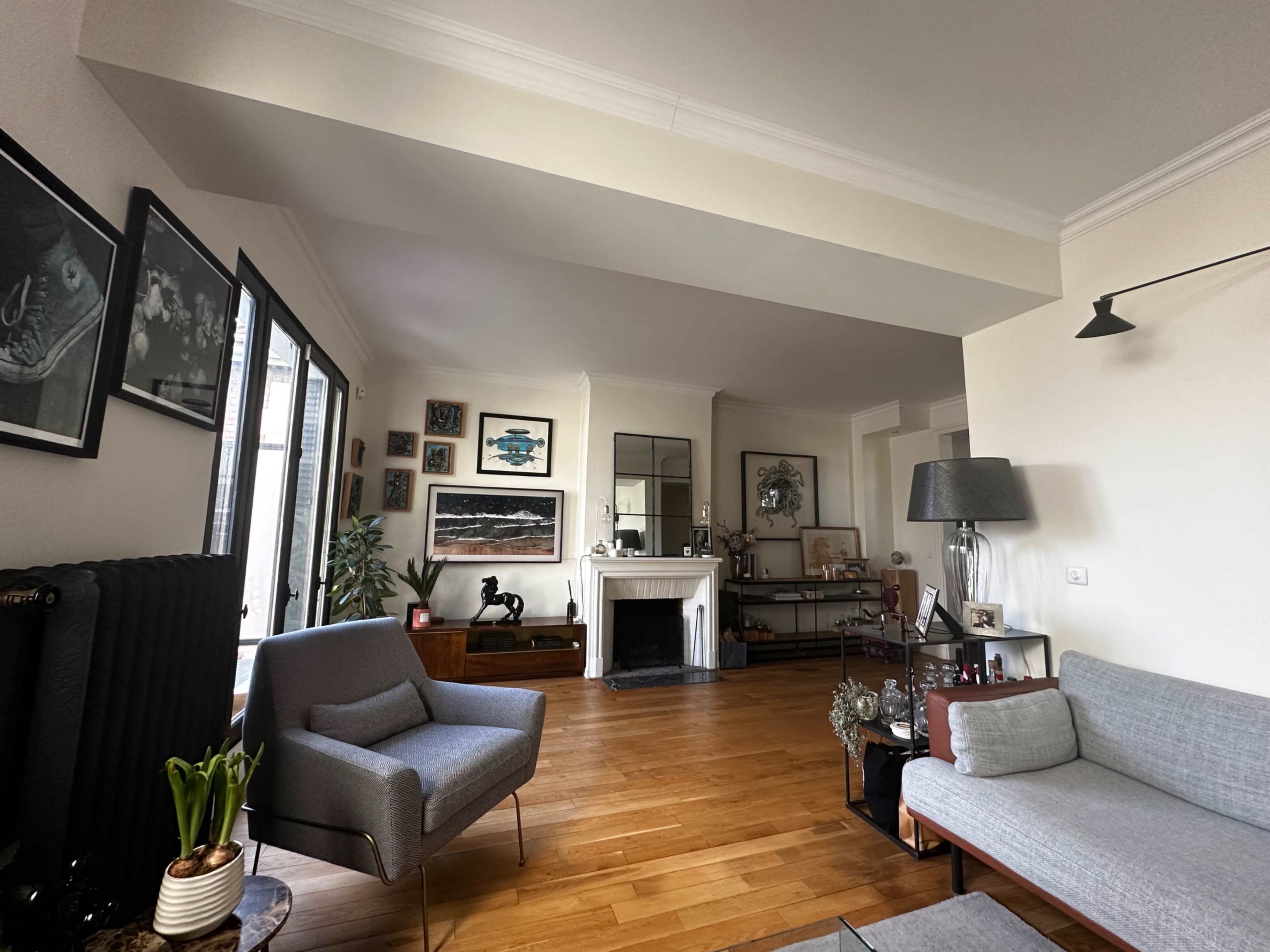 The image shows a well-lit living room featuring a mix of contemporary furniture, a fireplace, and various wall art pieces.