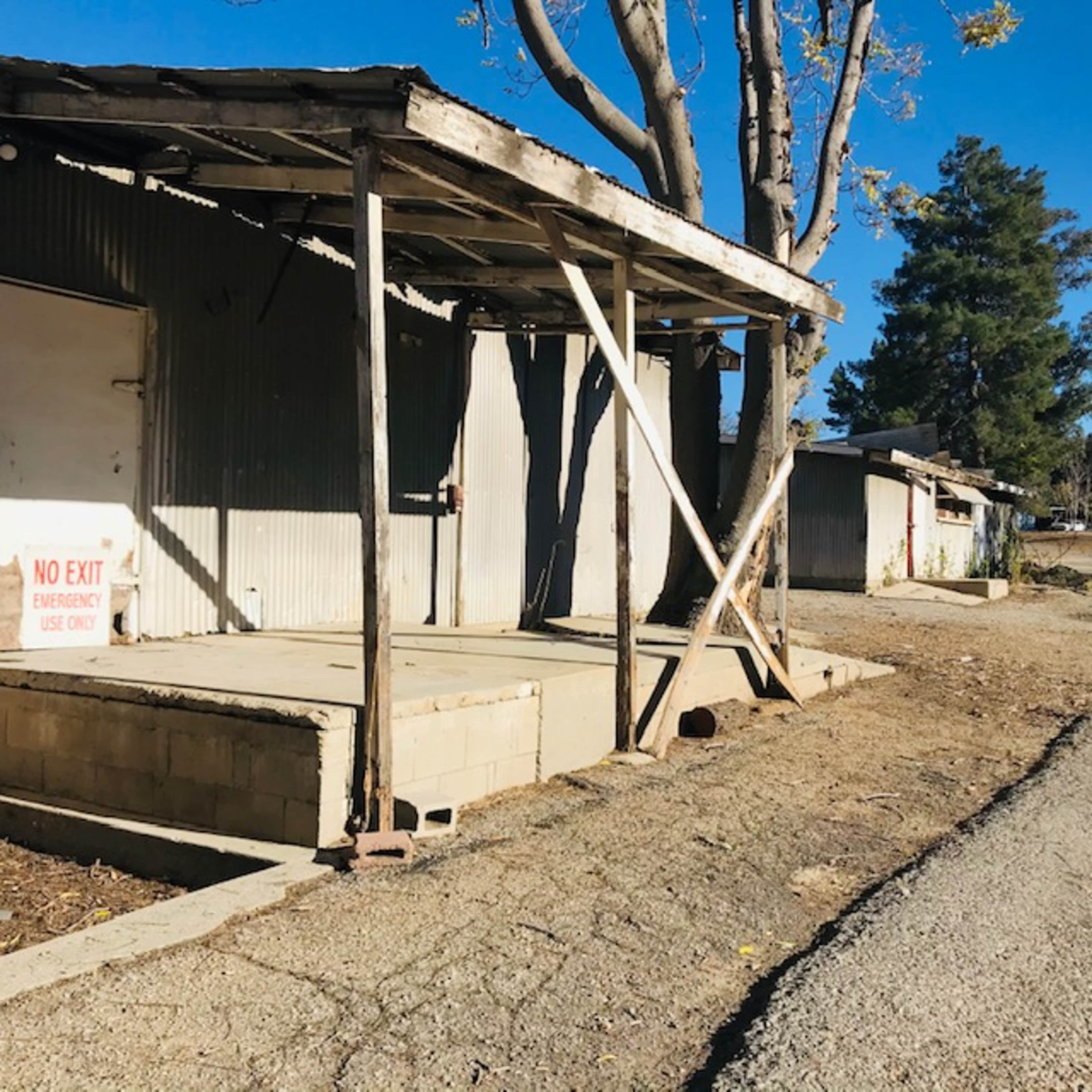 The image shows a weathered, abandoned loading dock with a "No Exit" sign and a dirt road alongside it.