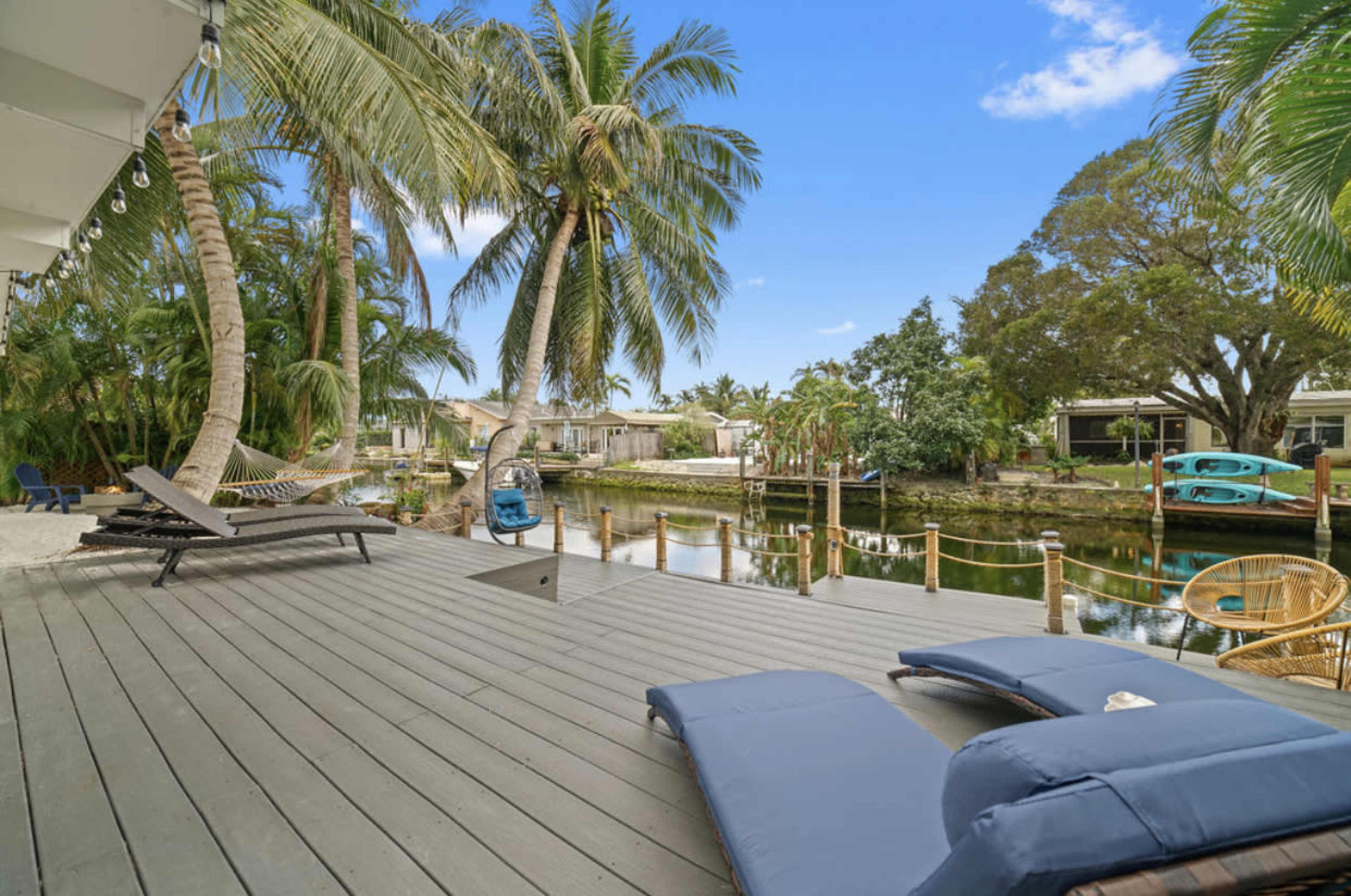 A deck with lounge chairs overlooking a canal lined with palm trees and houses.