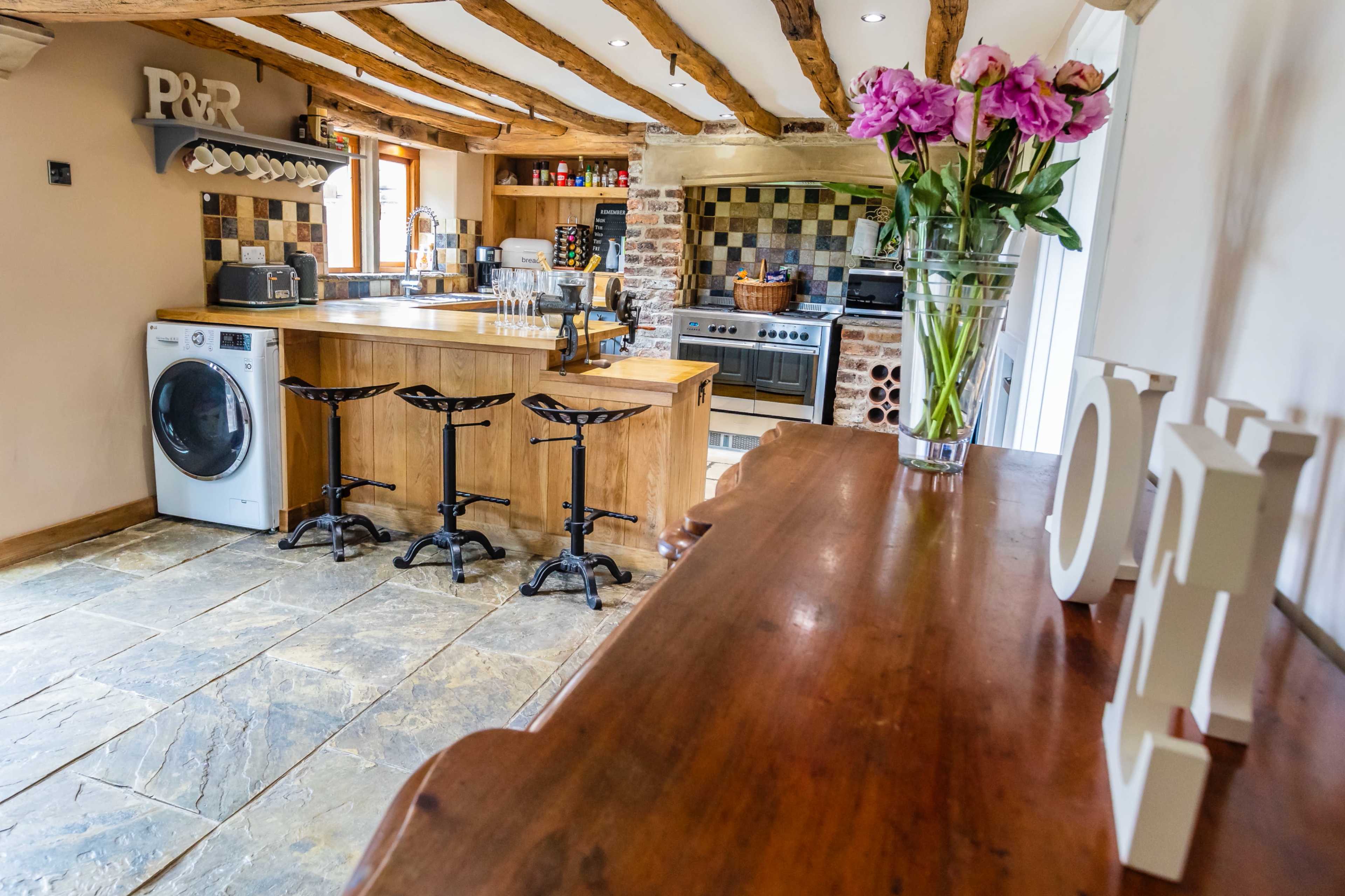 A rustic kitchen with wooden beams, a central island with bar stools, and a variety of appliances, including a washing machine and a stove.