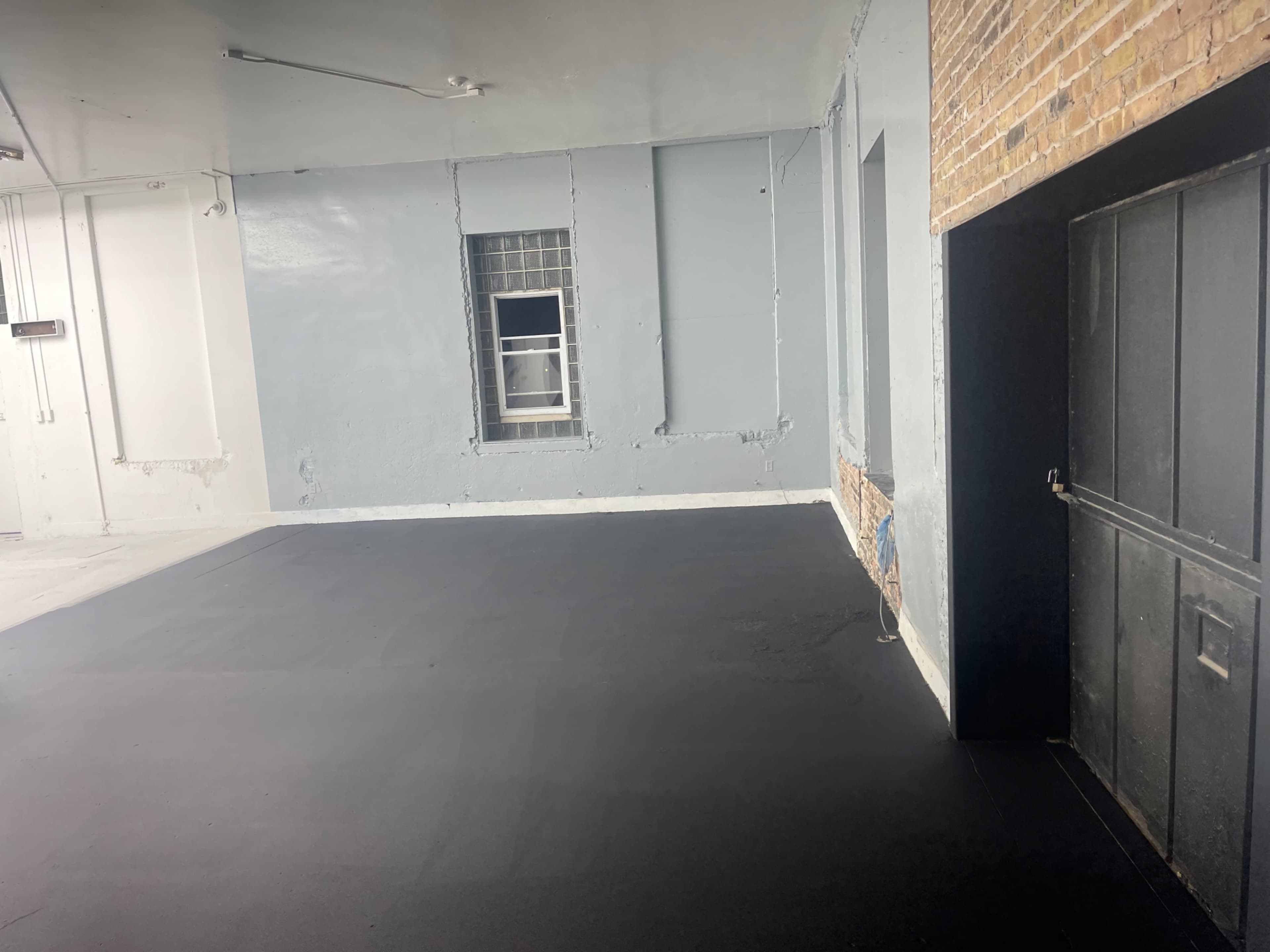 An empty room with gray walls and a dark floor, featuring a window and a doorway.