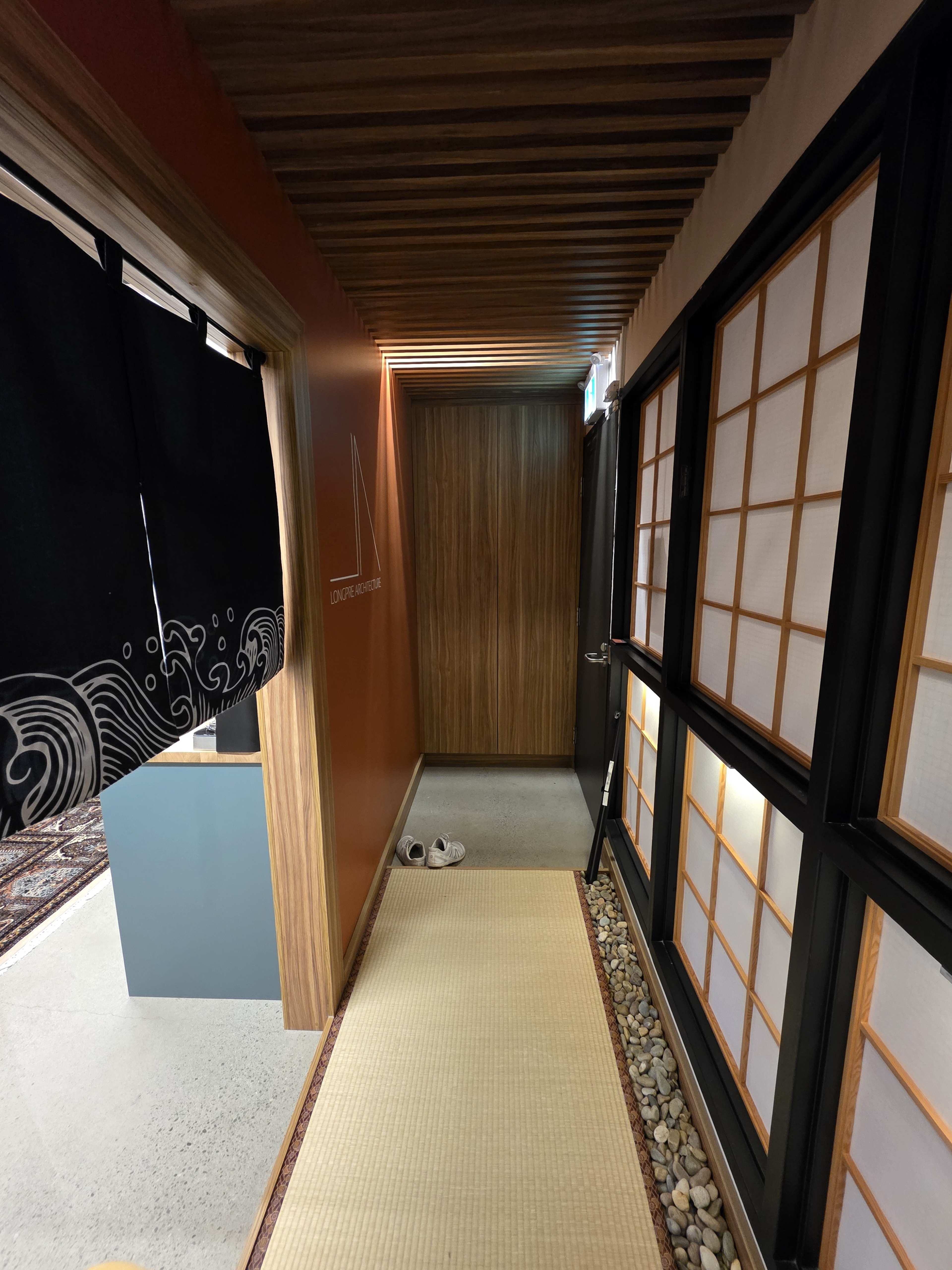 The image depicts a narrow hallway with wooden paneling, tatami flooring, and a Japanese-style sliding door on one side.