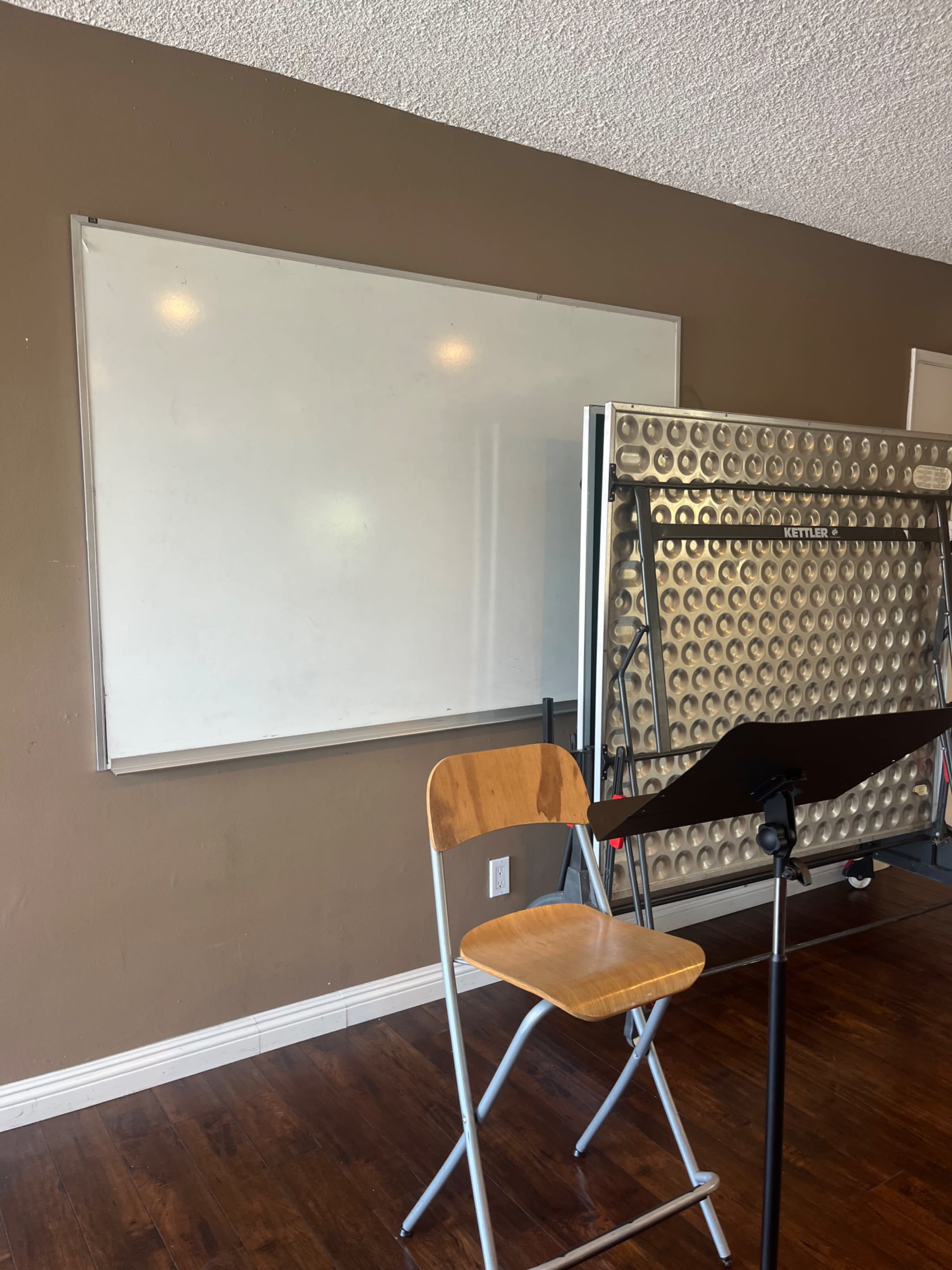 A whiteboard mounted on a wall next to a folding screen, with a wooden chair positioned in front of it.
