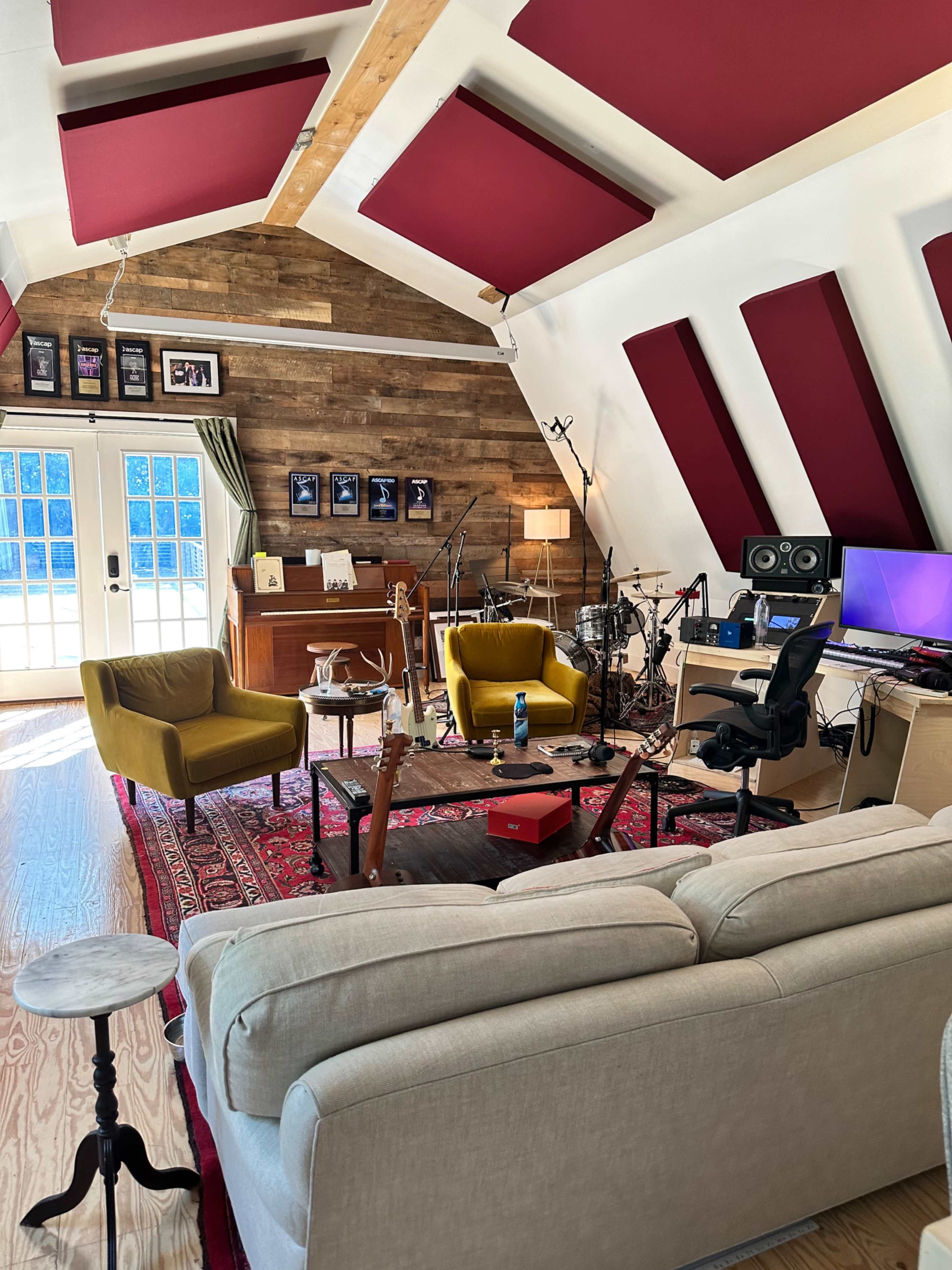 A music studio with a wooden floor, comfortable seating, a recording setup, and various musical instruments and decorations on the walls.