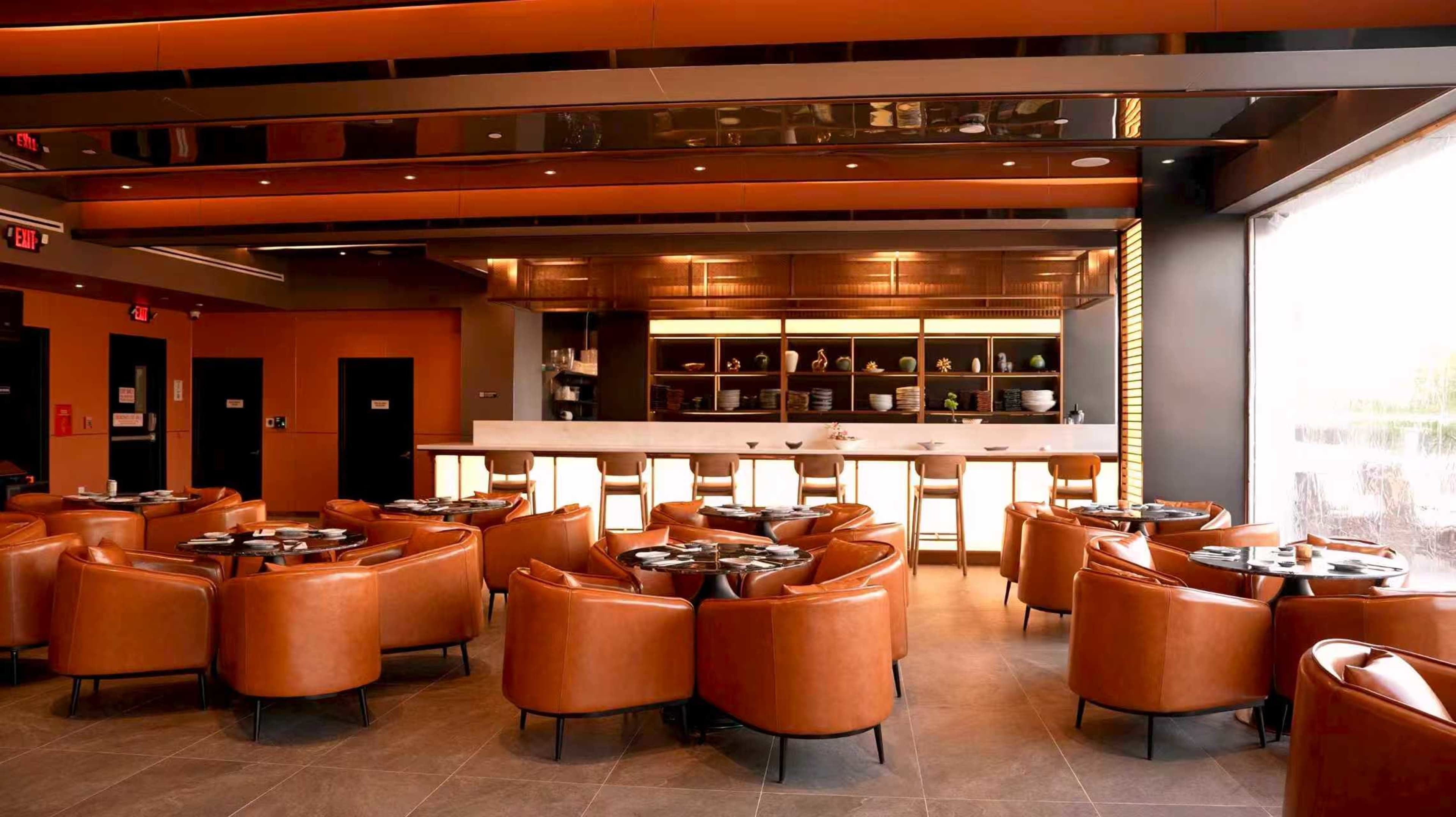 The image features a modern restaurant interior with brown leather seating and a sleek bar area illuminated by warm lighting.