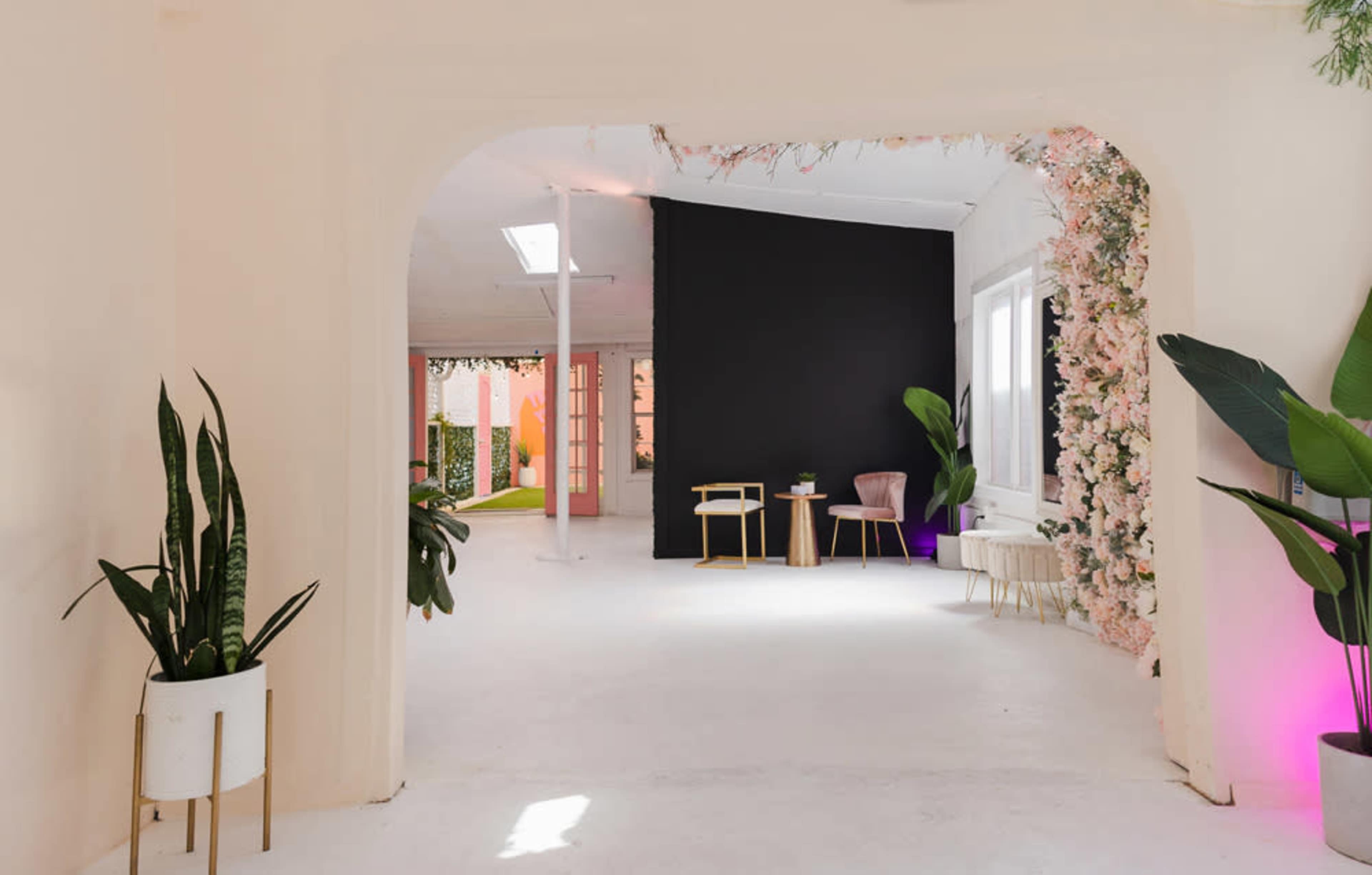 A bright, minimalist interior with an archway leading to a room featuring plants, neutral furniture, and colorful accent walls.