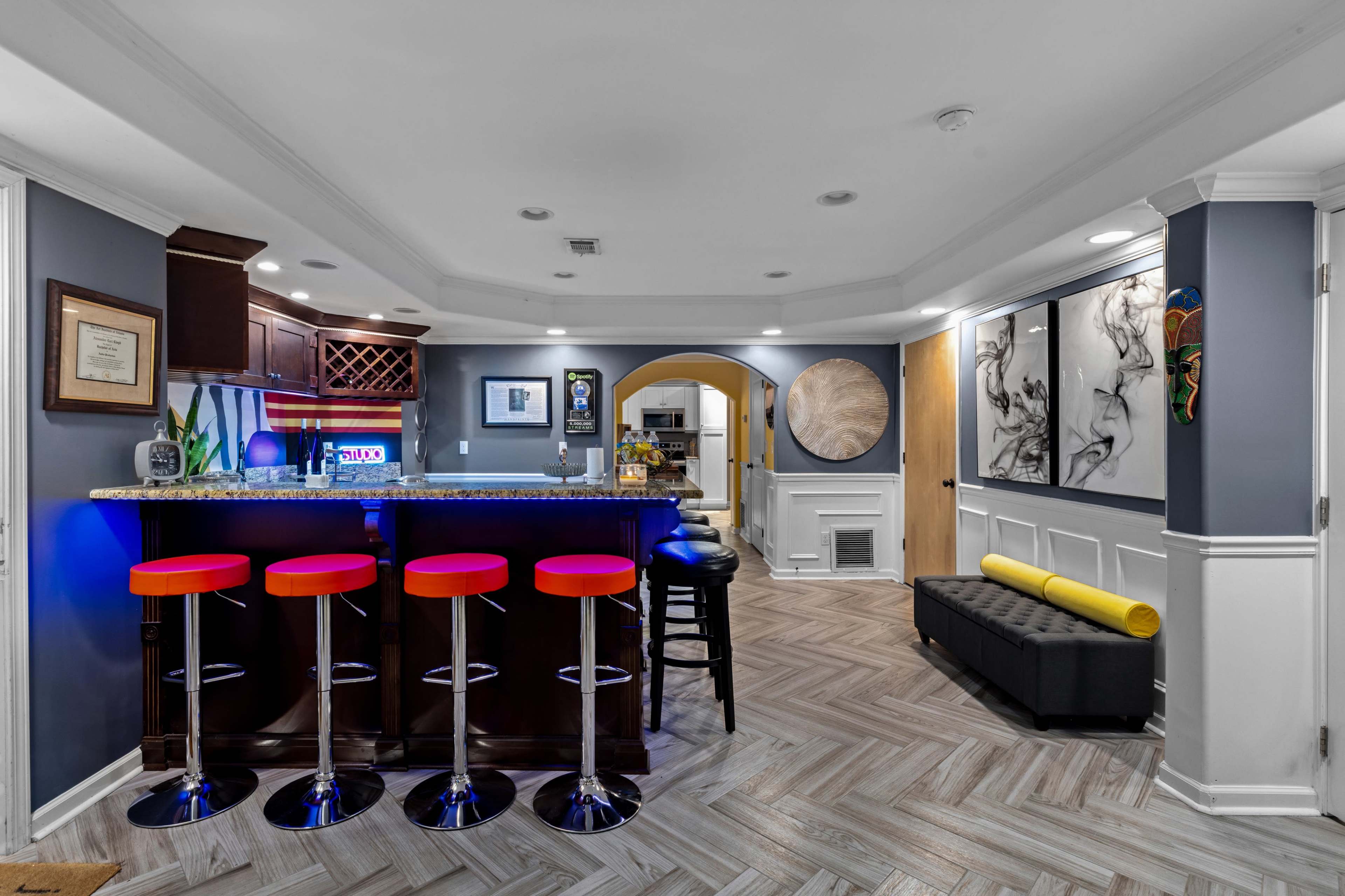 A modern basement bar area featuring four red bar stools, dark cabinetry, and an artistic wall display.