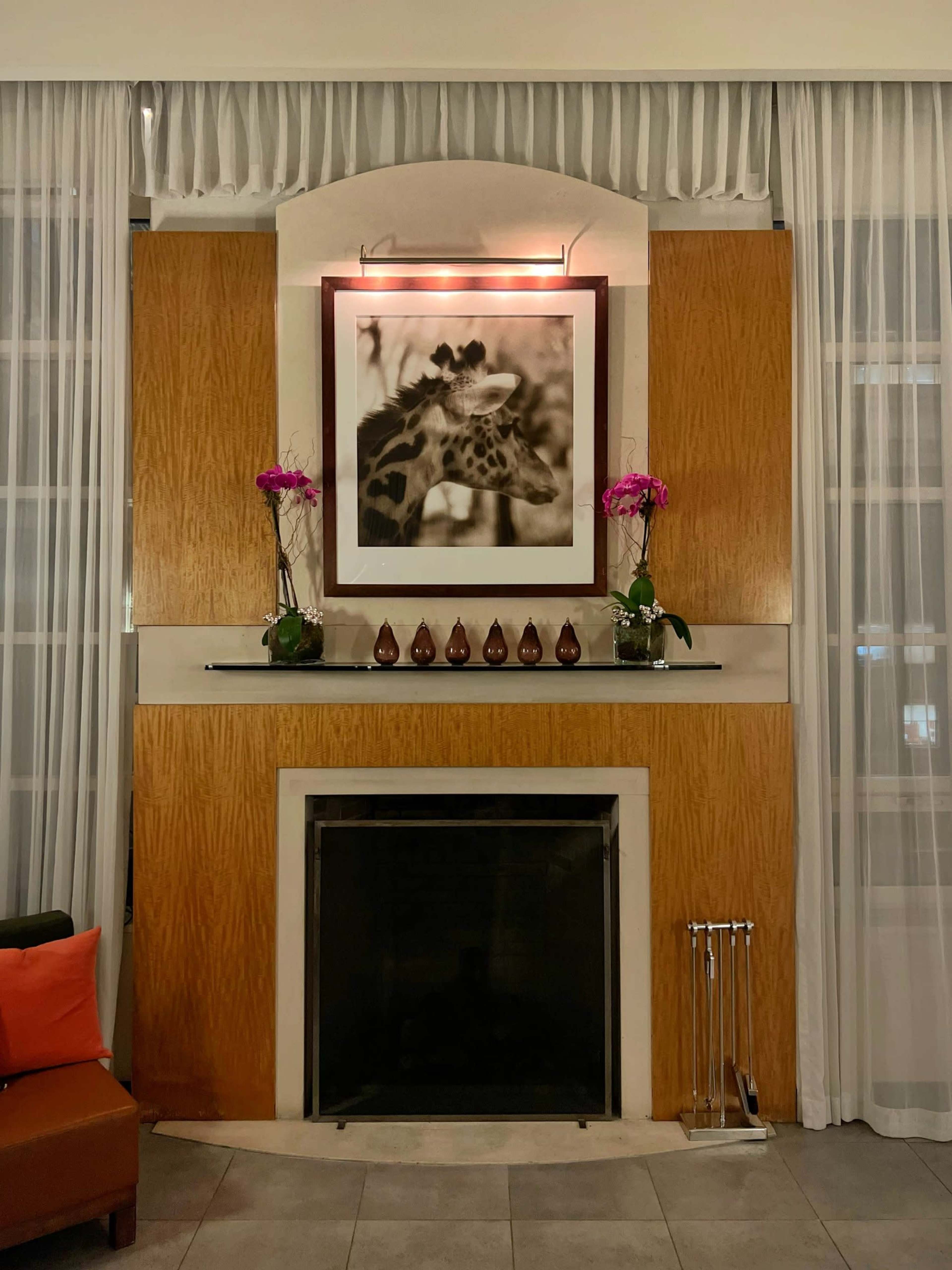 The image shows a decorative fireplace surrounded by a wooden wall, with a large black-and-white giraffe photograph and several potted orchids above the mantel.
