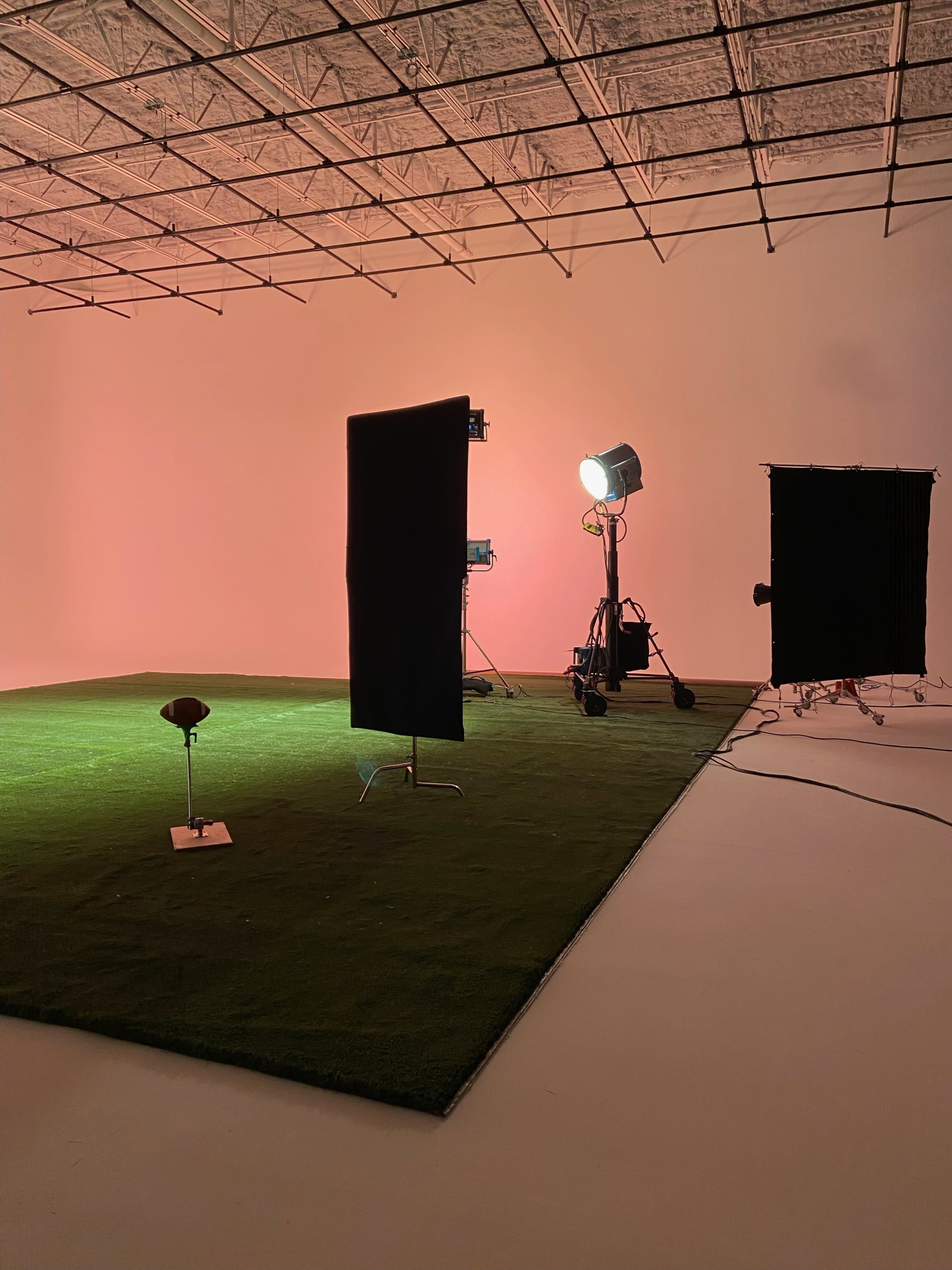 A studio with green artificial grass flooring, black backdrops, and lighting equipment set up for a photo shoot.