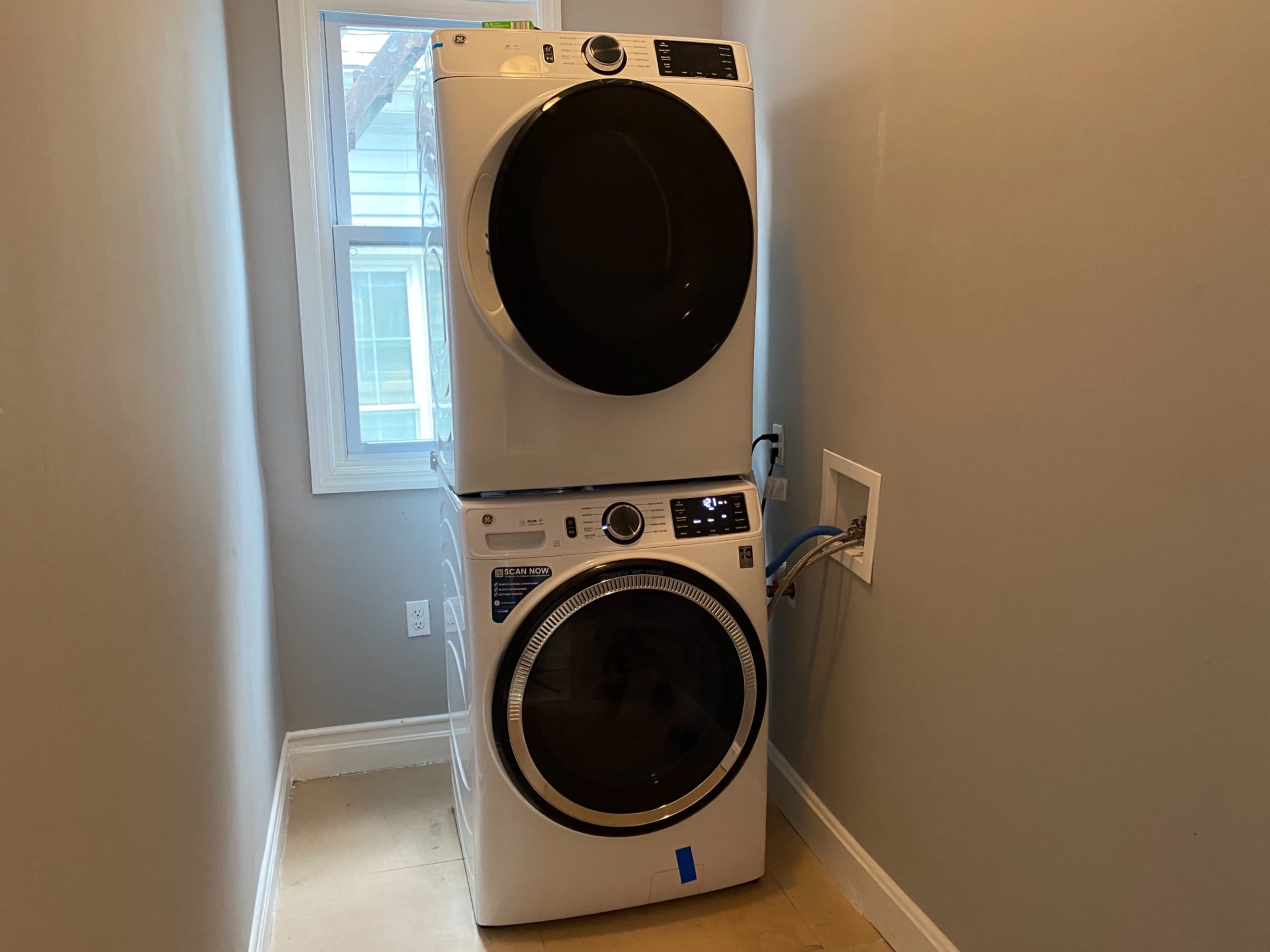 A stacked washer and dryer are installed in a small laundry area next to a window.