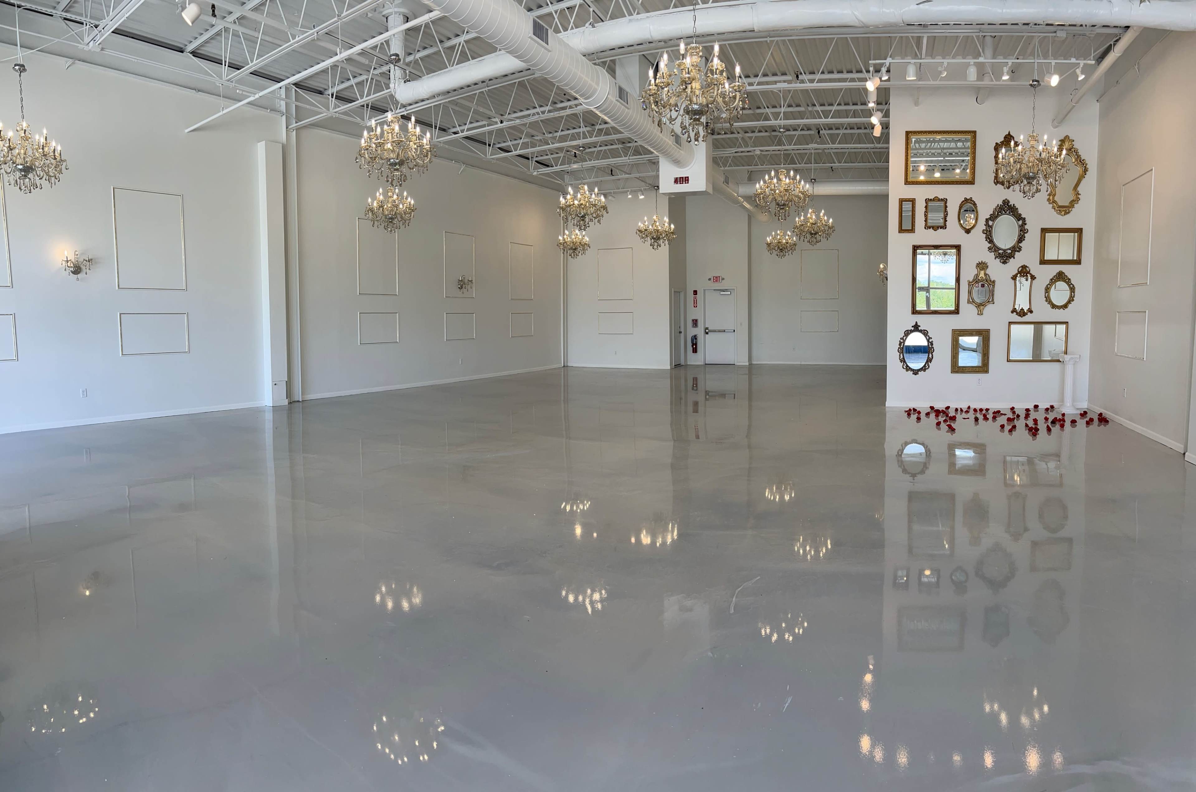 The image shows a spacious, empty room with polished concrete floors, multiple hanging chandeliers, and decorative mirrors mounted on the walls.
