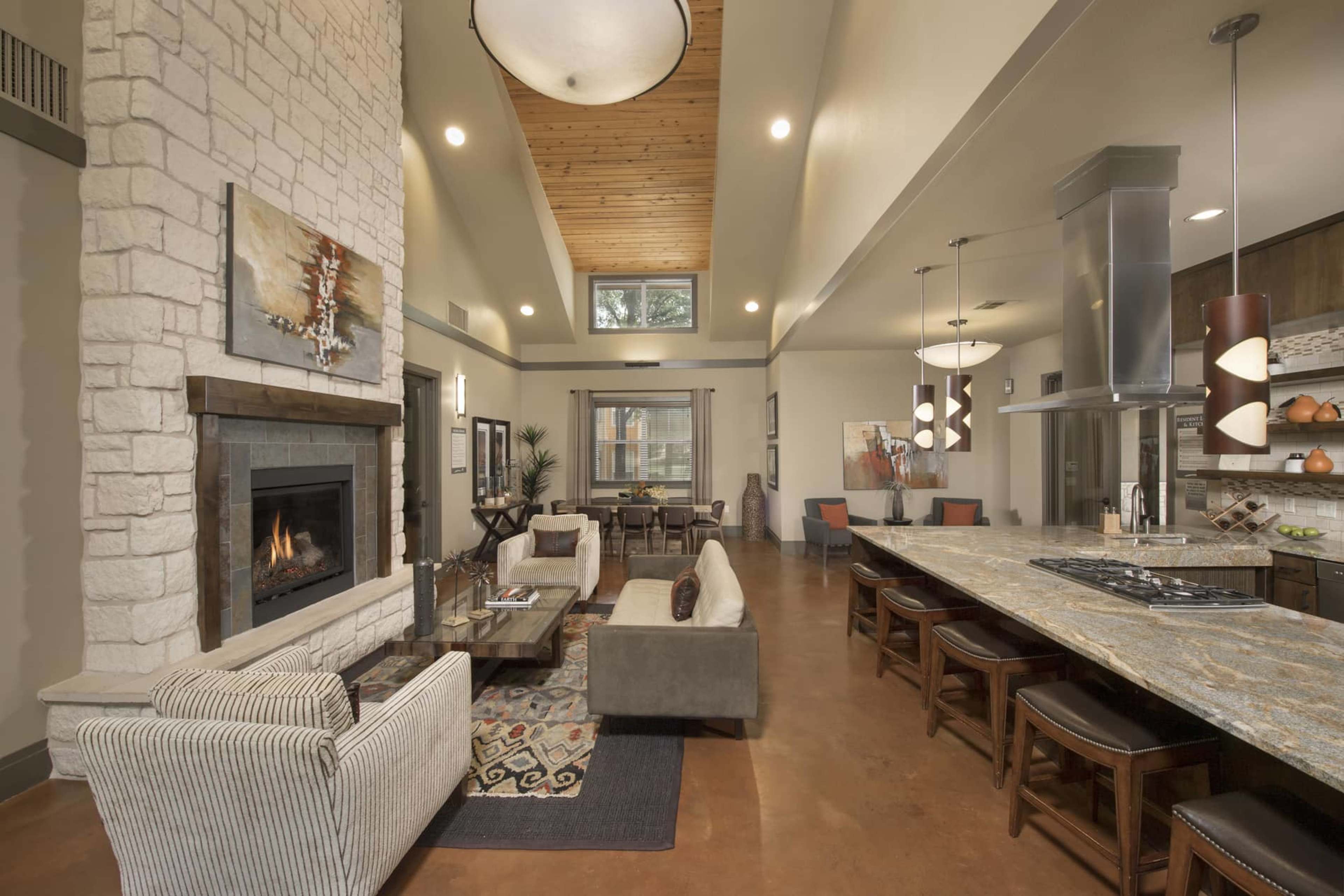 A modern living space features a stone fireplace, a large kitchen island with seating, and a mix of cozy furniture arranged around the room.