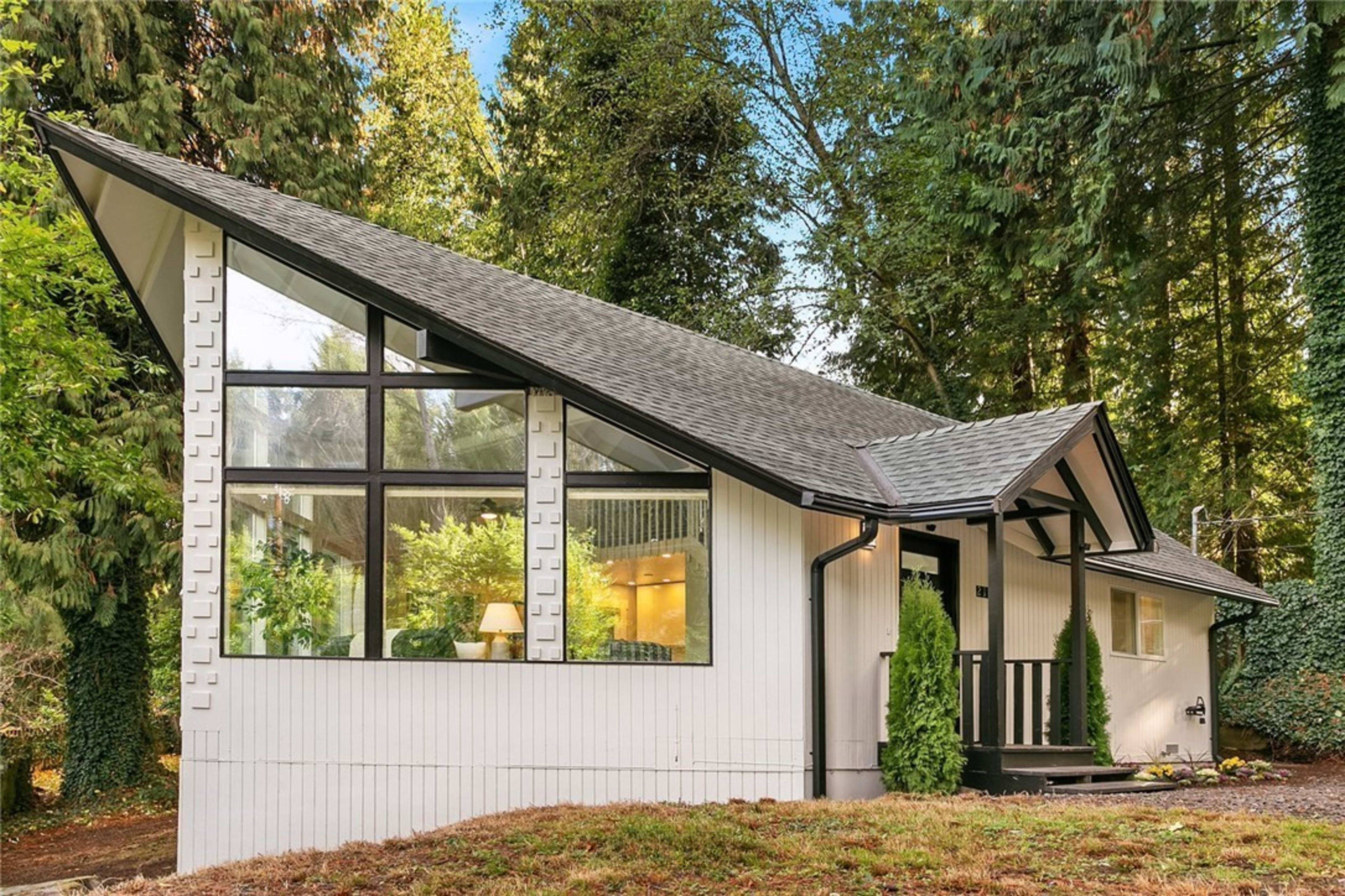 A modern house with a distinctive angular roof and large windows, set among tall trees in a forested area.