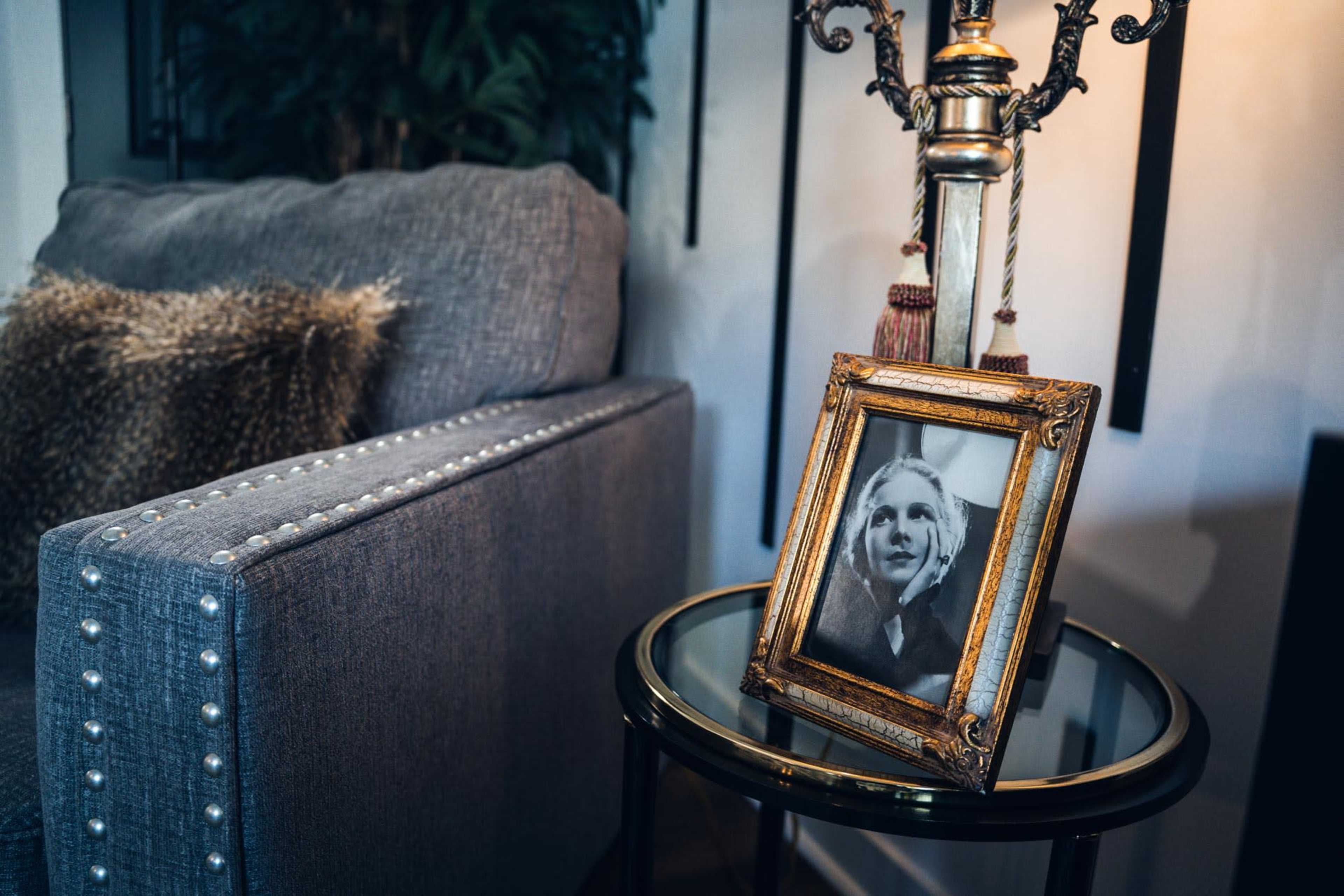 A decorative lamp stands next to a gray couch, with a framed black-and-white photo on a glass side table.
