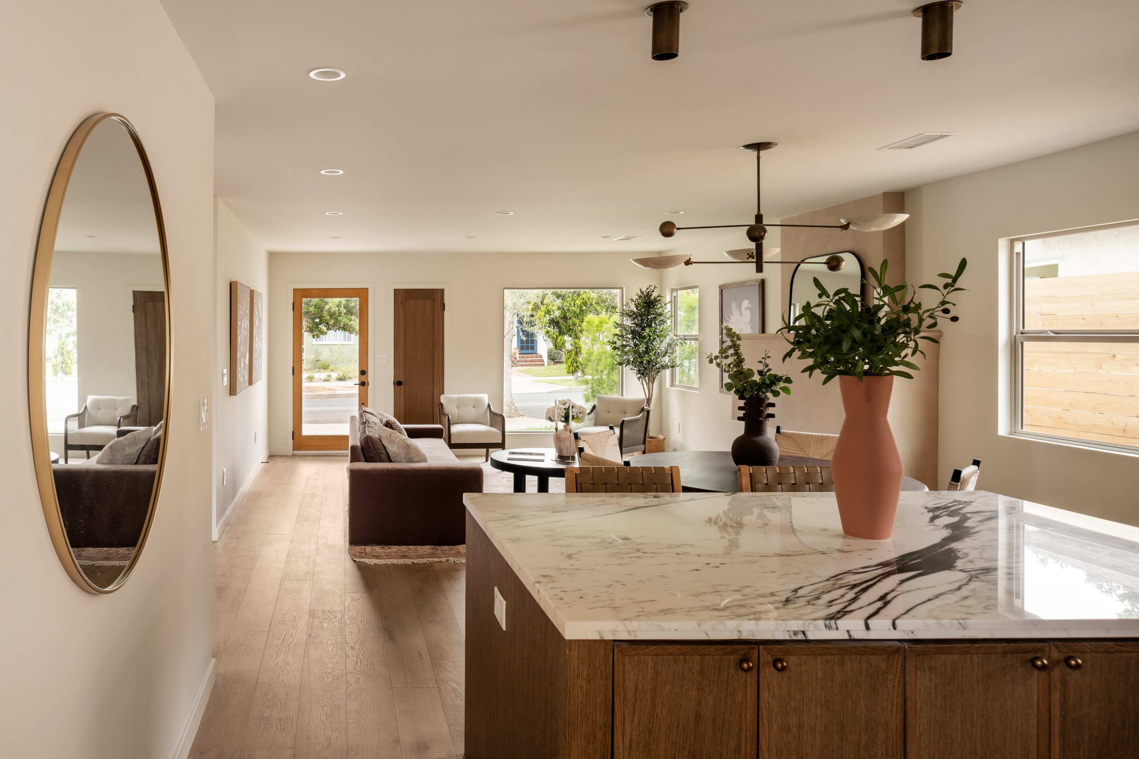A modern open-concept living space featuring a kitchen island with a marble top, a living area with seating, and large windows allowing natural light.