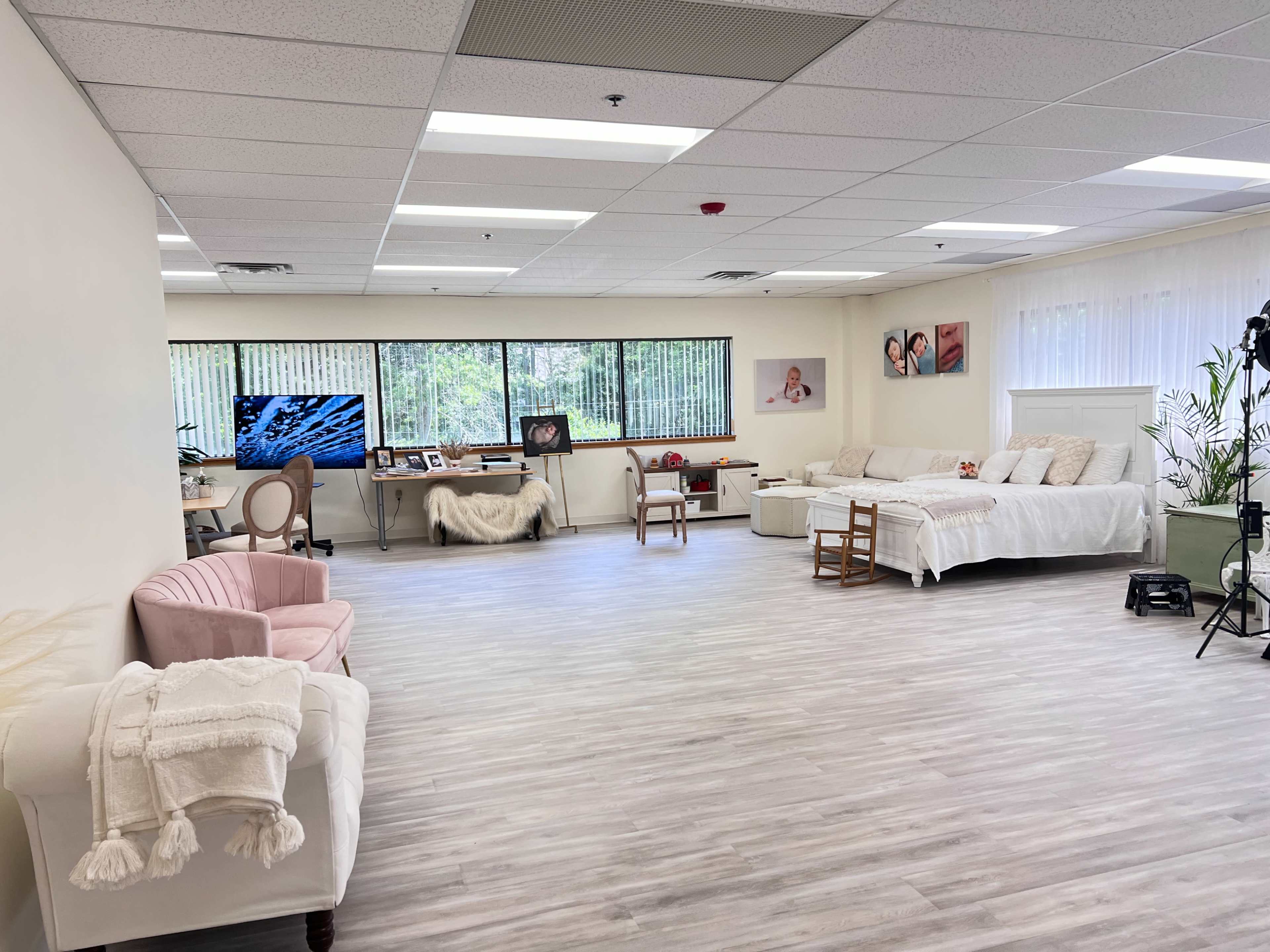 The image shows a spacious, well-lit room with a light-colored floor, featuring a couple of couches, a desk with a computer, and decorative artwork on the walls.