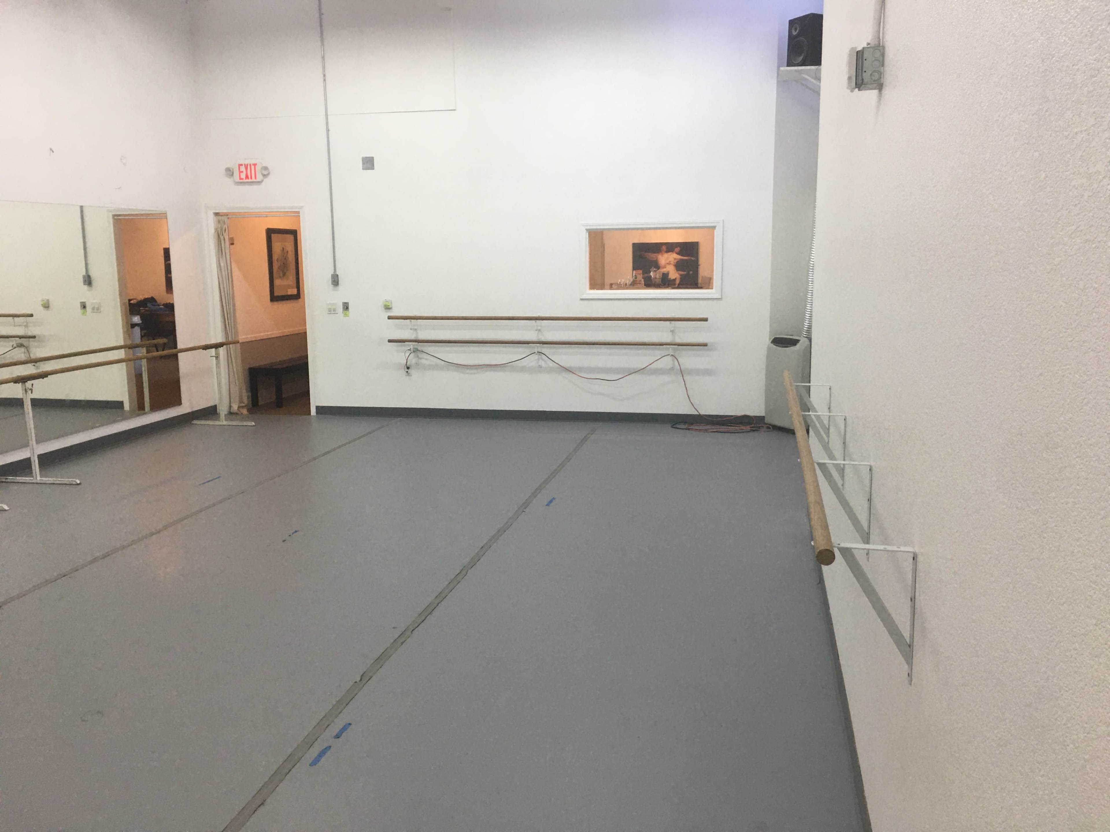 A dance studio with a mirrored wall, wooden barre installed along the walls, and a framed picture hanging on the far wall.