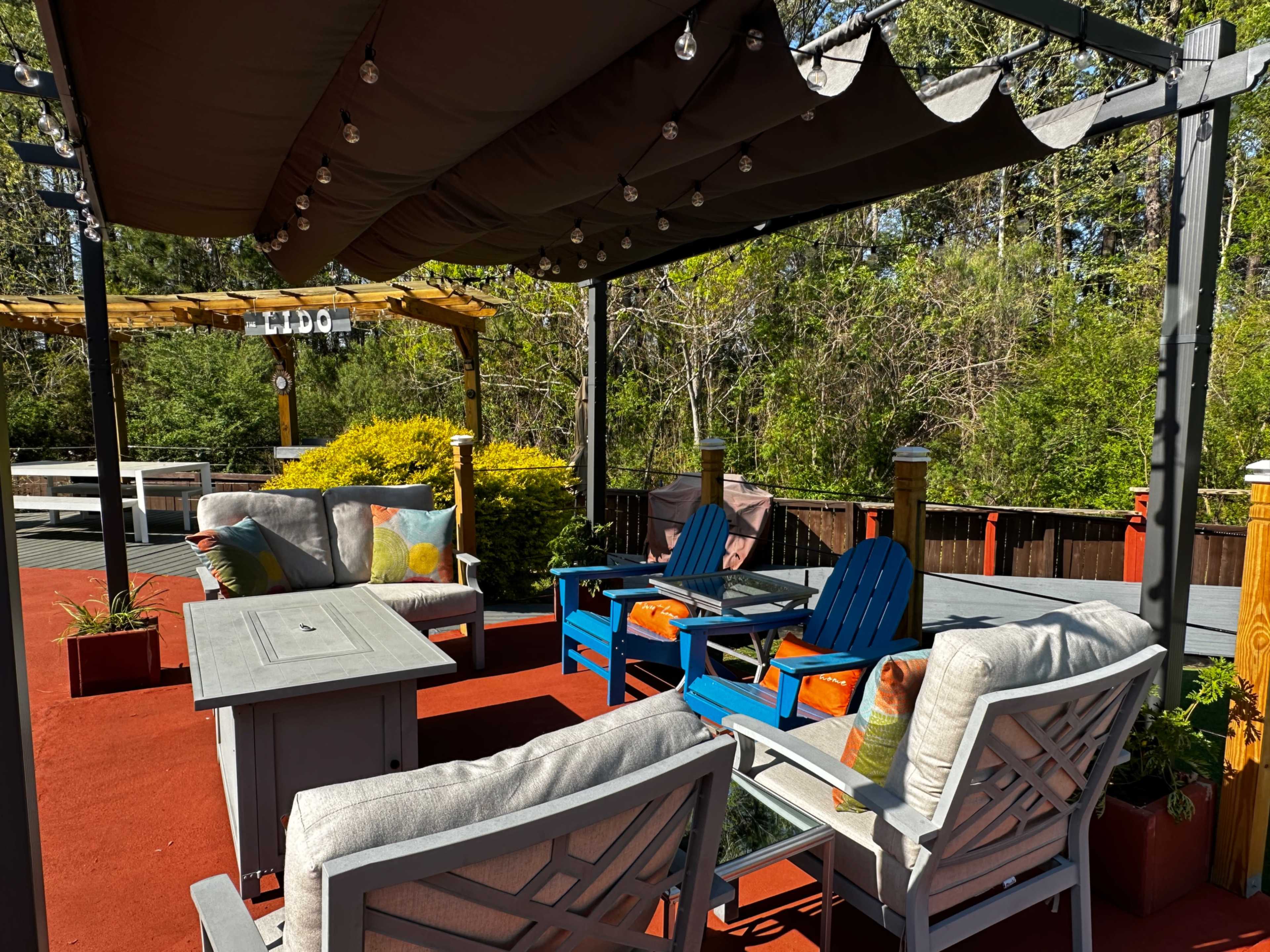 The image shows a patio area with several outdoor seating arrangements, including colorful chairs and a table, under a shaded pergola.