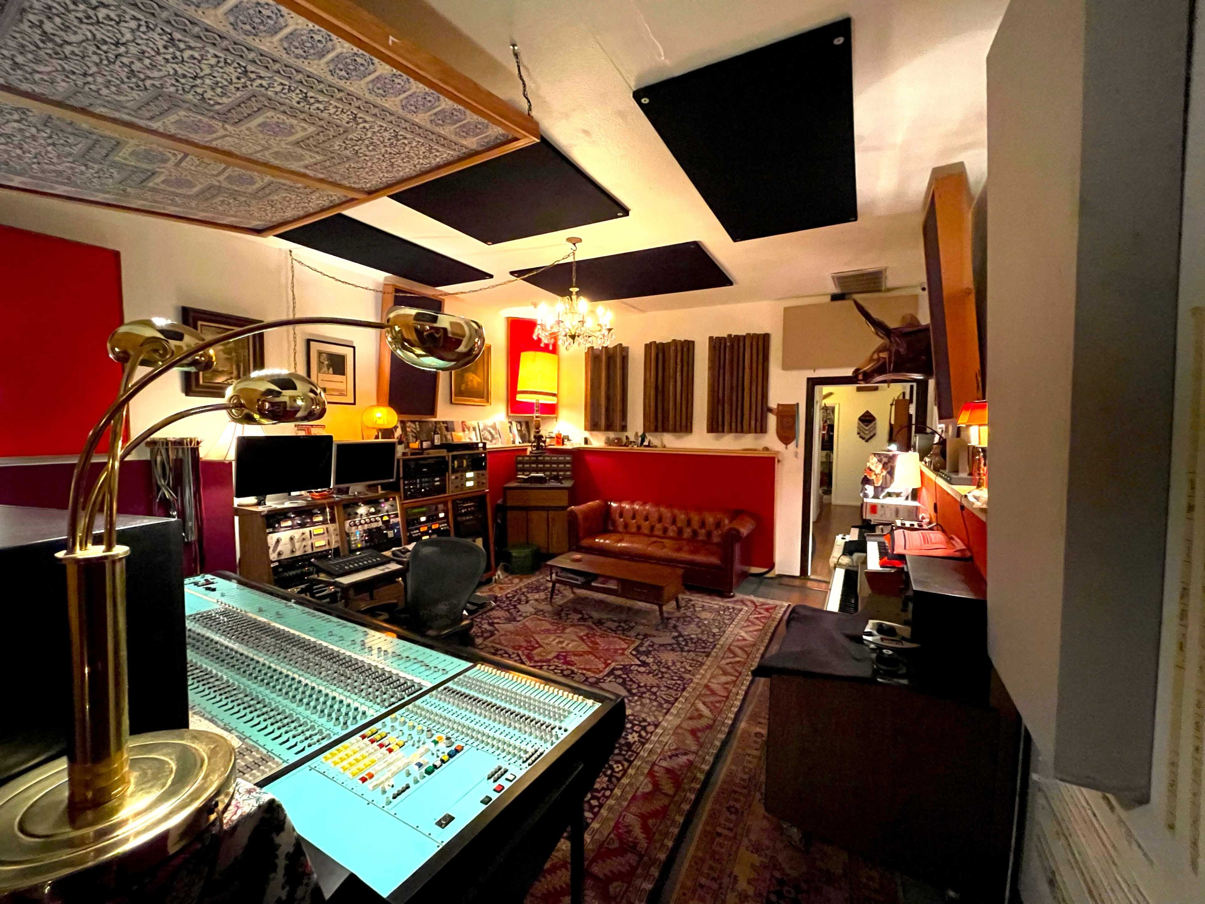 A music studio features a mixing console, vintage furnishings, soundproofing panels, and various recording equipment.