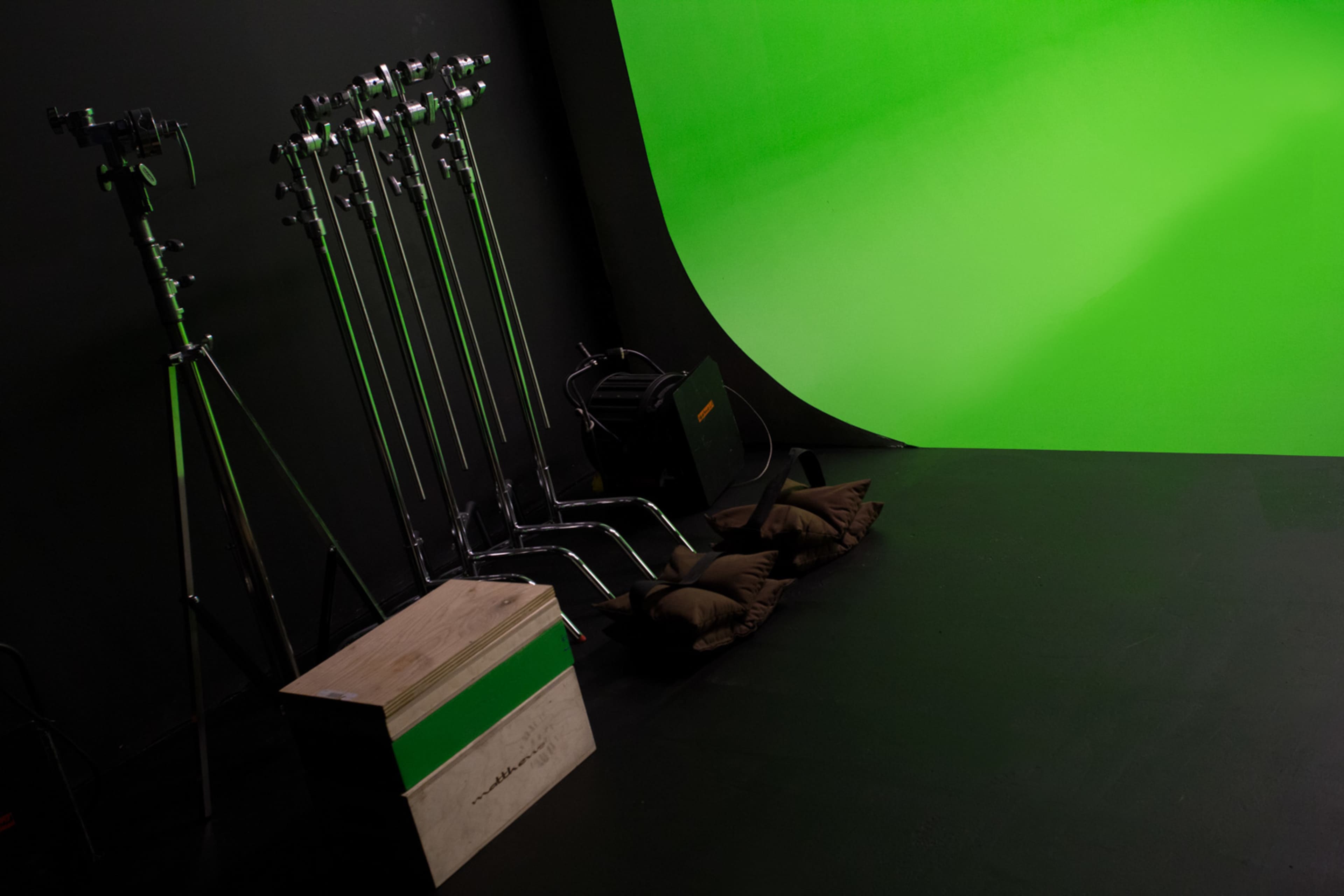 A studio setup featuring a green backdrop, light stands, and two cushions on the floor.
