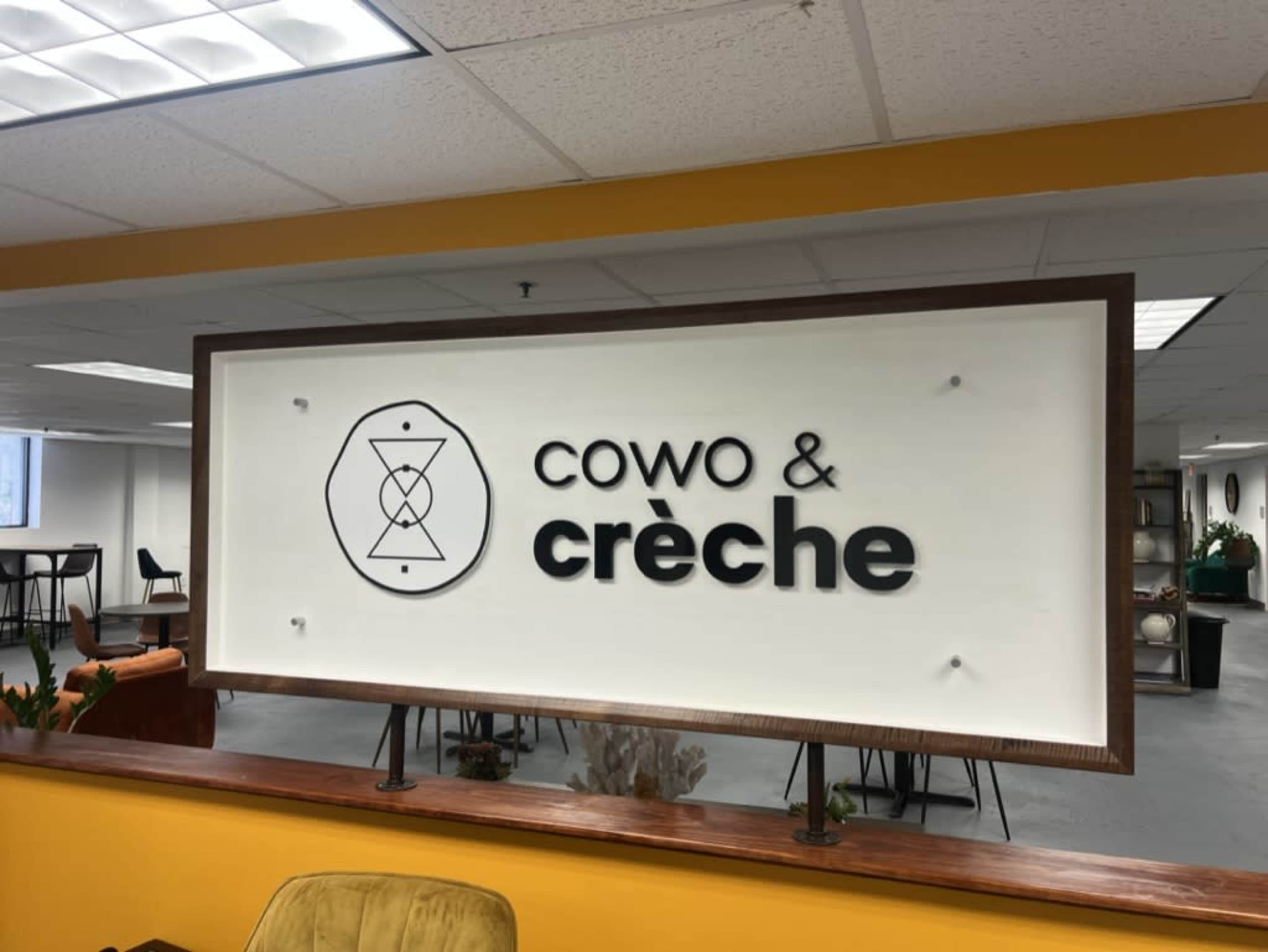 The image shows a large sign reading "Cowo & crèche" set against a bright yellow wall in an indoor space.