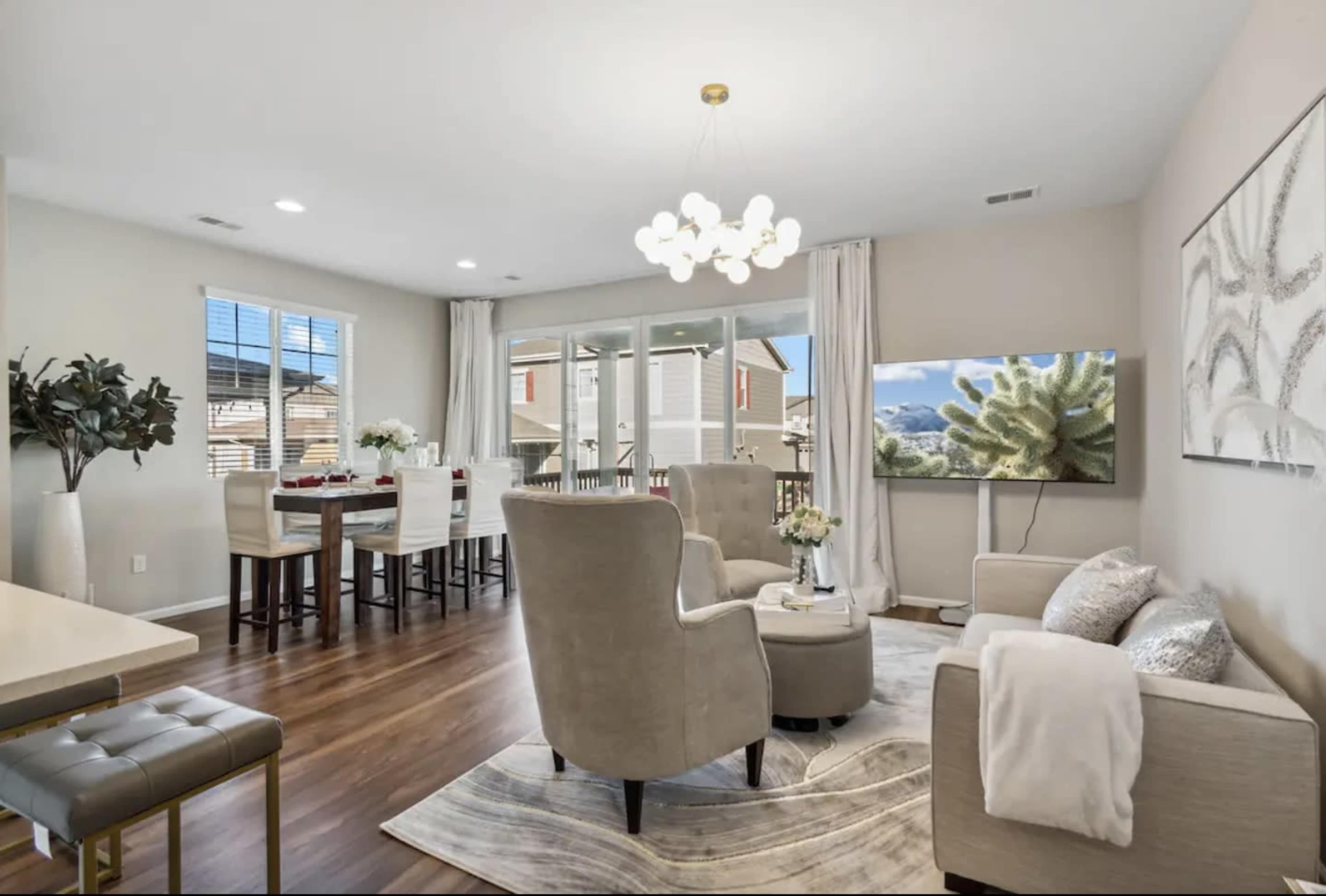 The image shows a modern living and dining area featuring seating, a coffee table, and a large television.