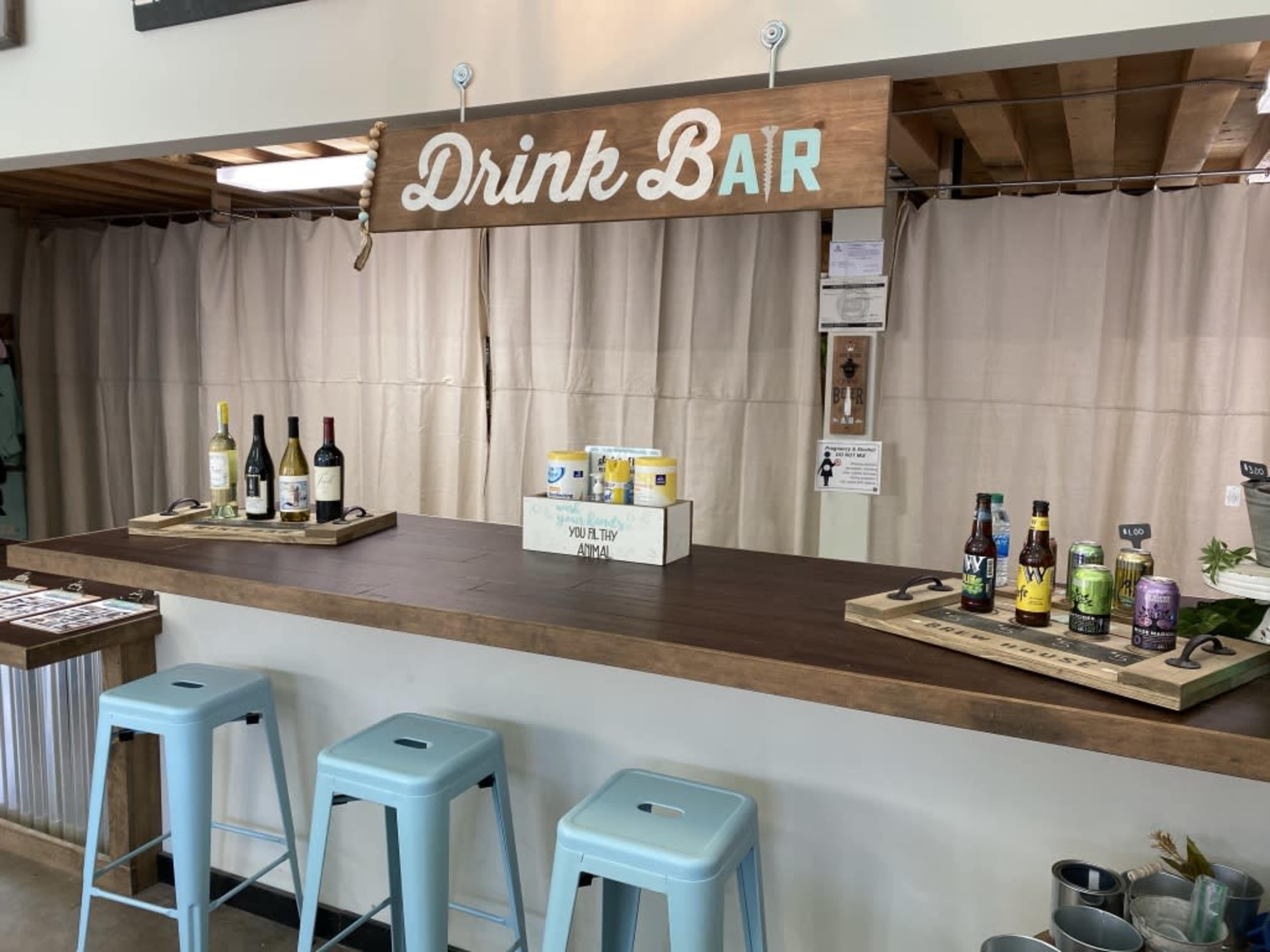 A drink bar with various bottles of wine and craft beverages displayed on wooden trays, under a sign that reads "Drink Bar."