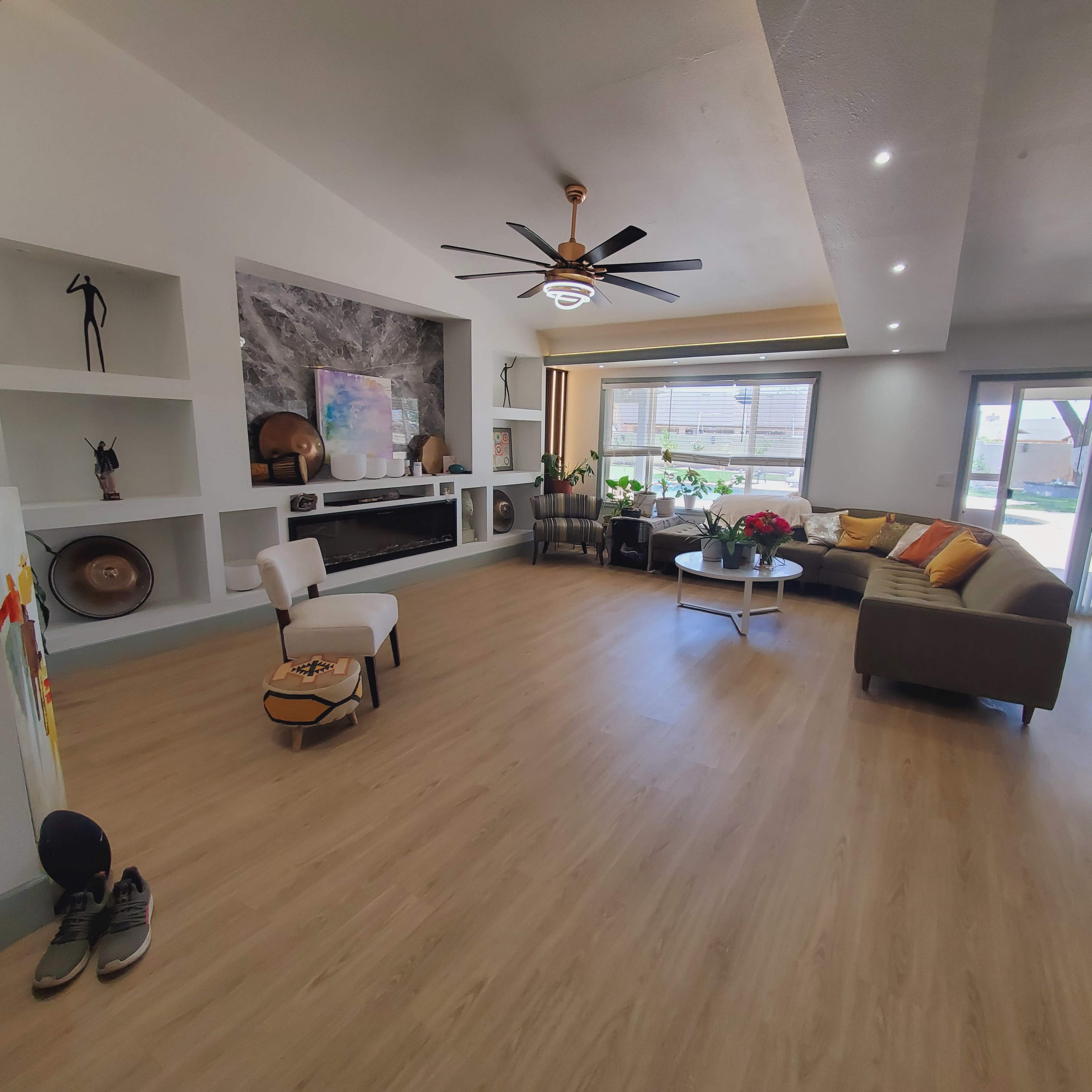 The image shows a spacious living room featuring a ceiling fan, a round coffee table, a sectional sofa, and a large wall-mounted television.