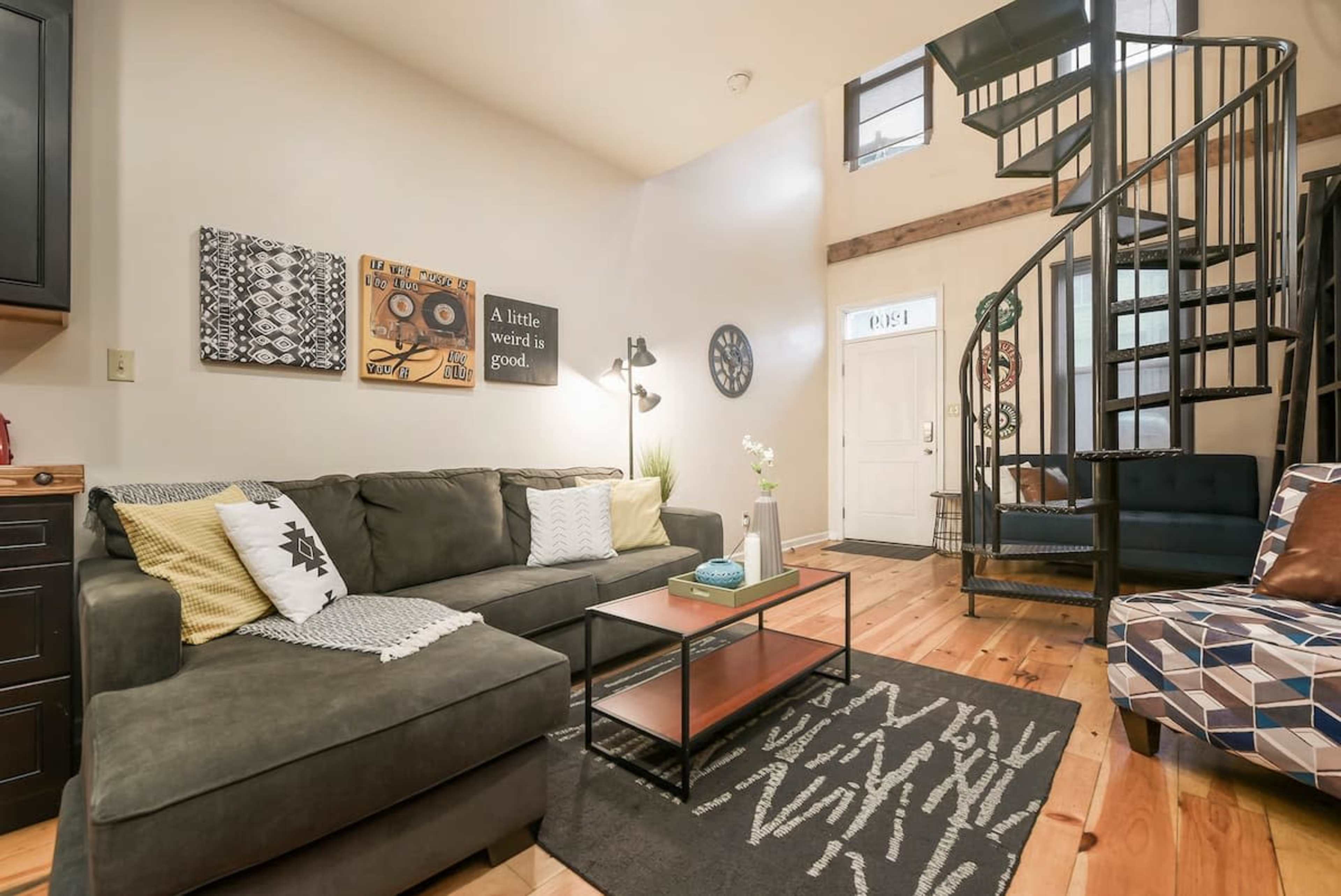 A cozy living room with a dark sofa, a coffee table, and a spiral staircase leading to an upper level.