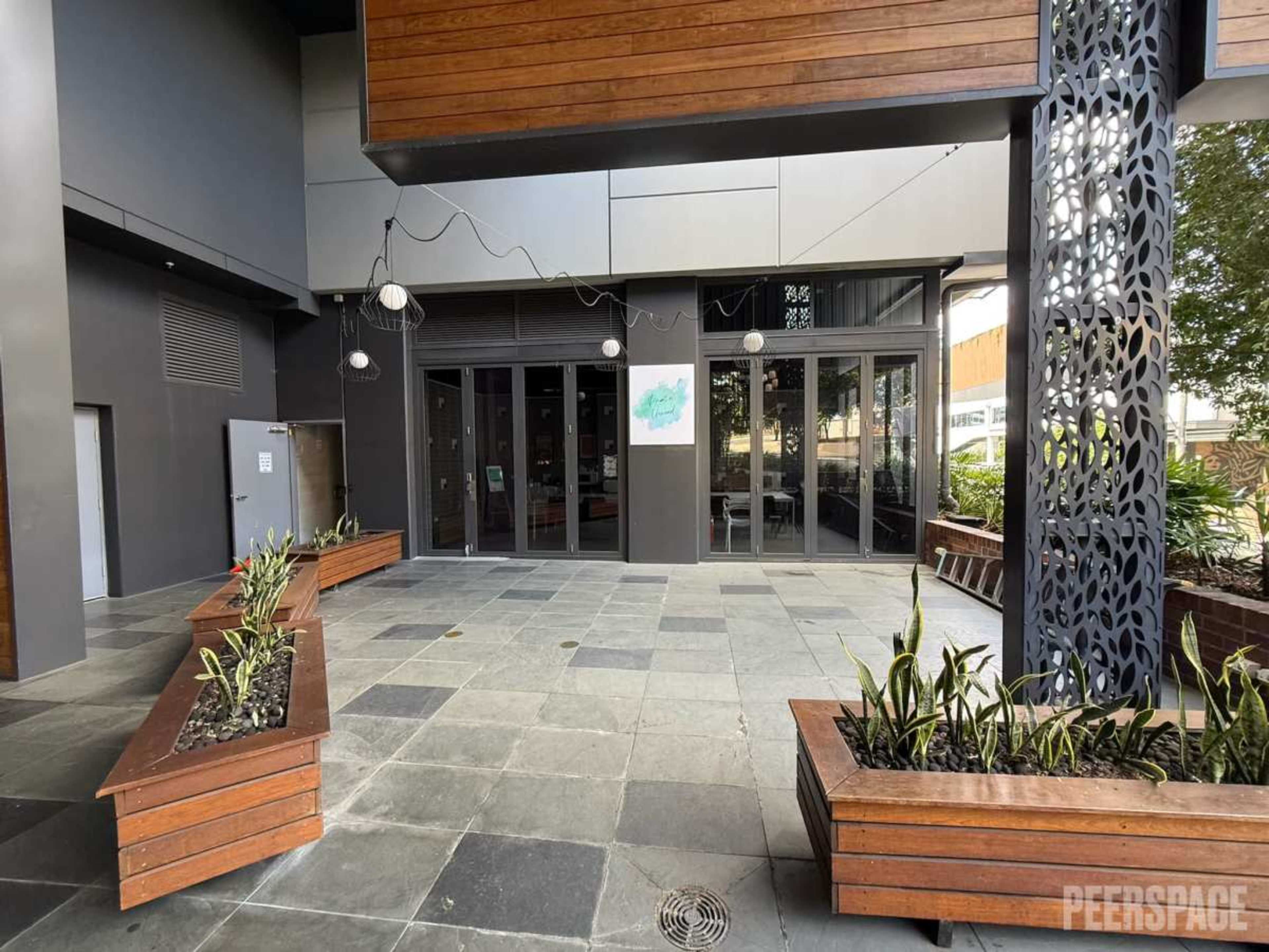 The image shows an entryway with large glass doors, surrounded by potted plants and a decorative wall element.