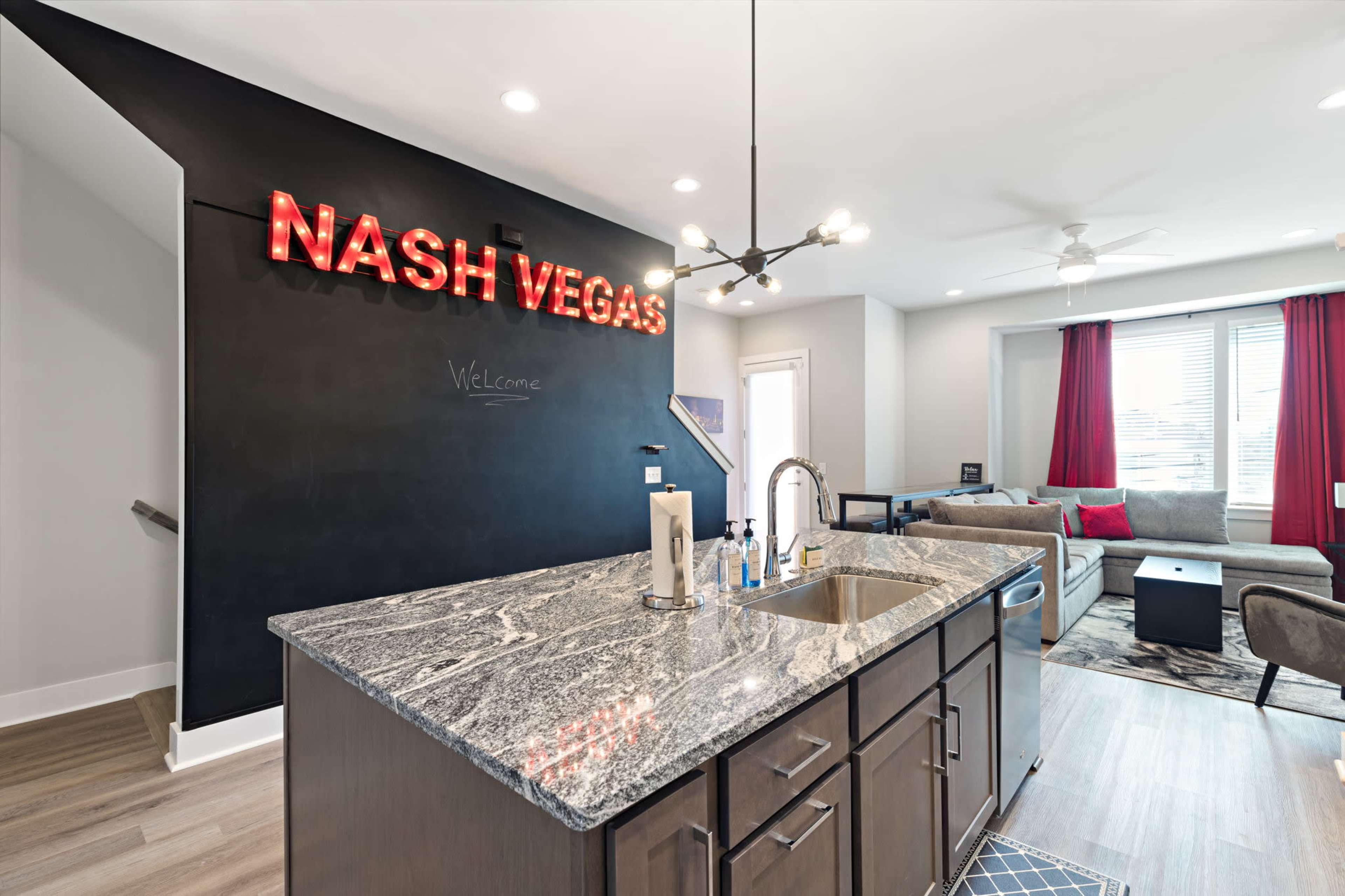 The image shows a modern kitchen with a dark countertop, a sink, and a prominent wall displaying the words "NASH VEGAS" in illuminated letters.