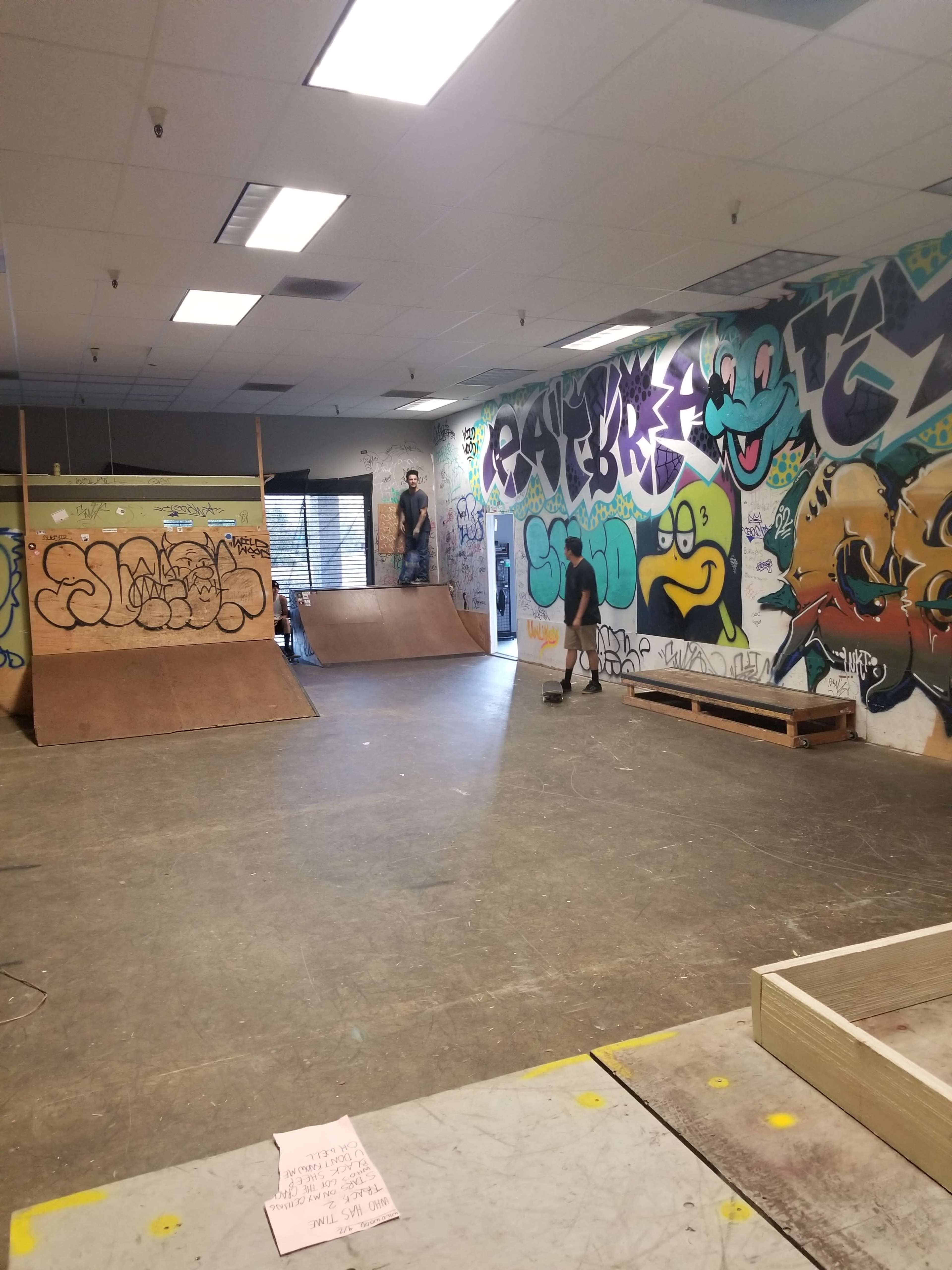 An indoor skate park with wooden ramps and colorful graffiti-covered walls.