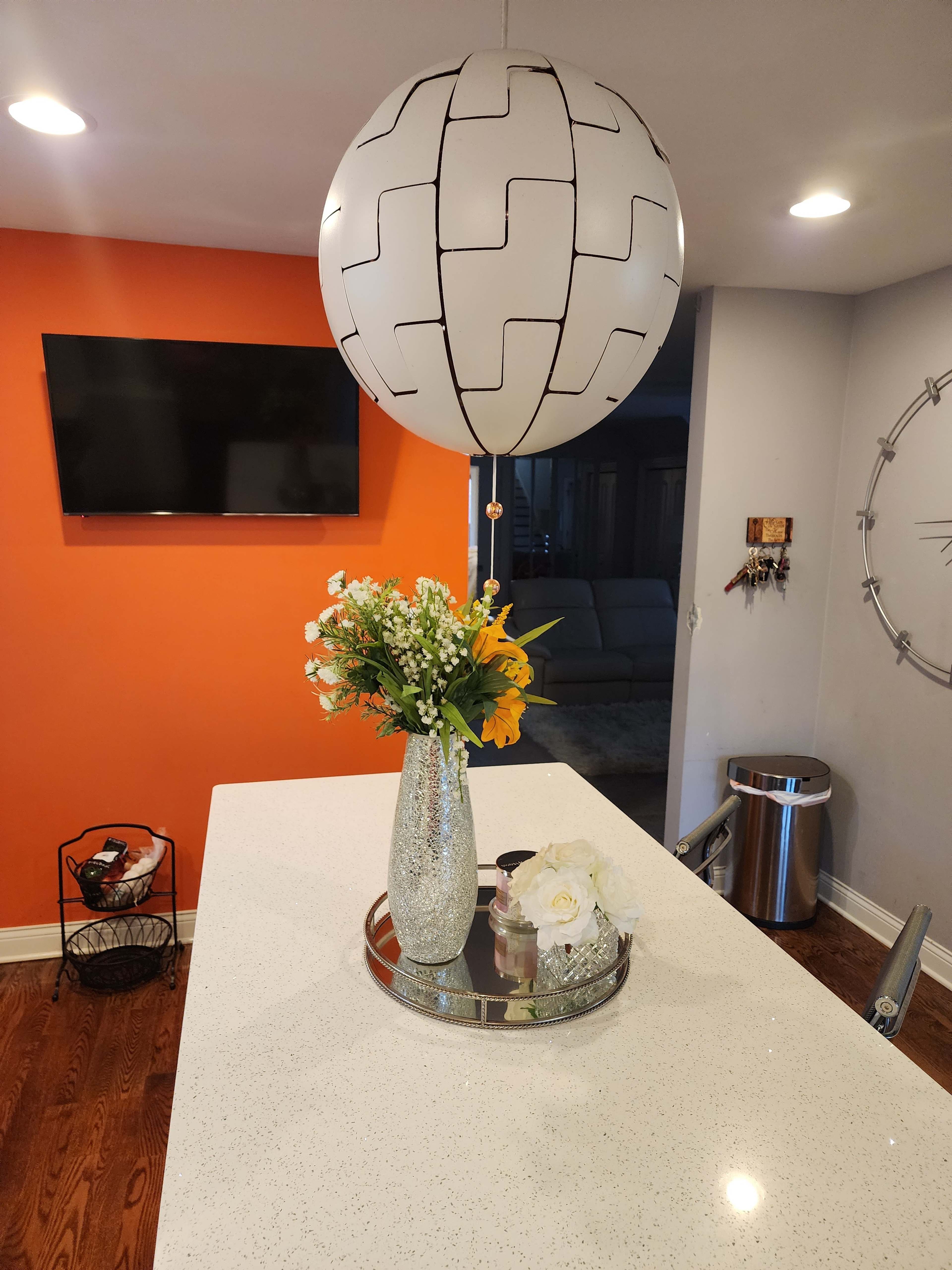 A modern kitchen features a round pendant light hanging above a countertop with a floral arrangement on a mirrored tray.