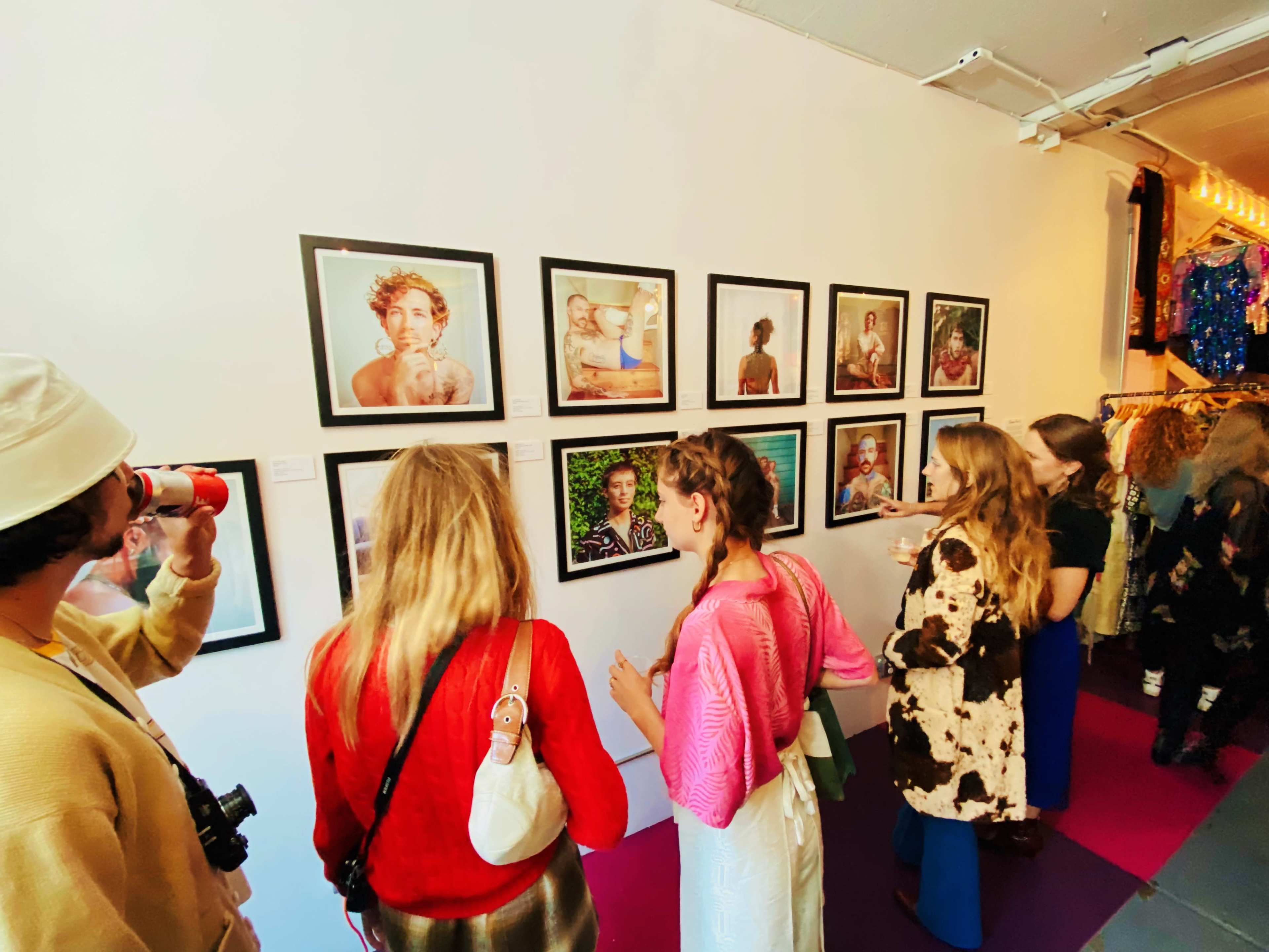 A group of people examines framed photographs displayed on a gallery wall.