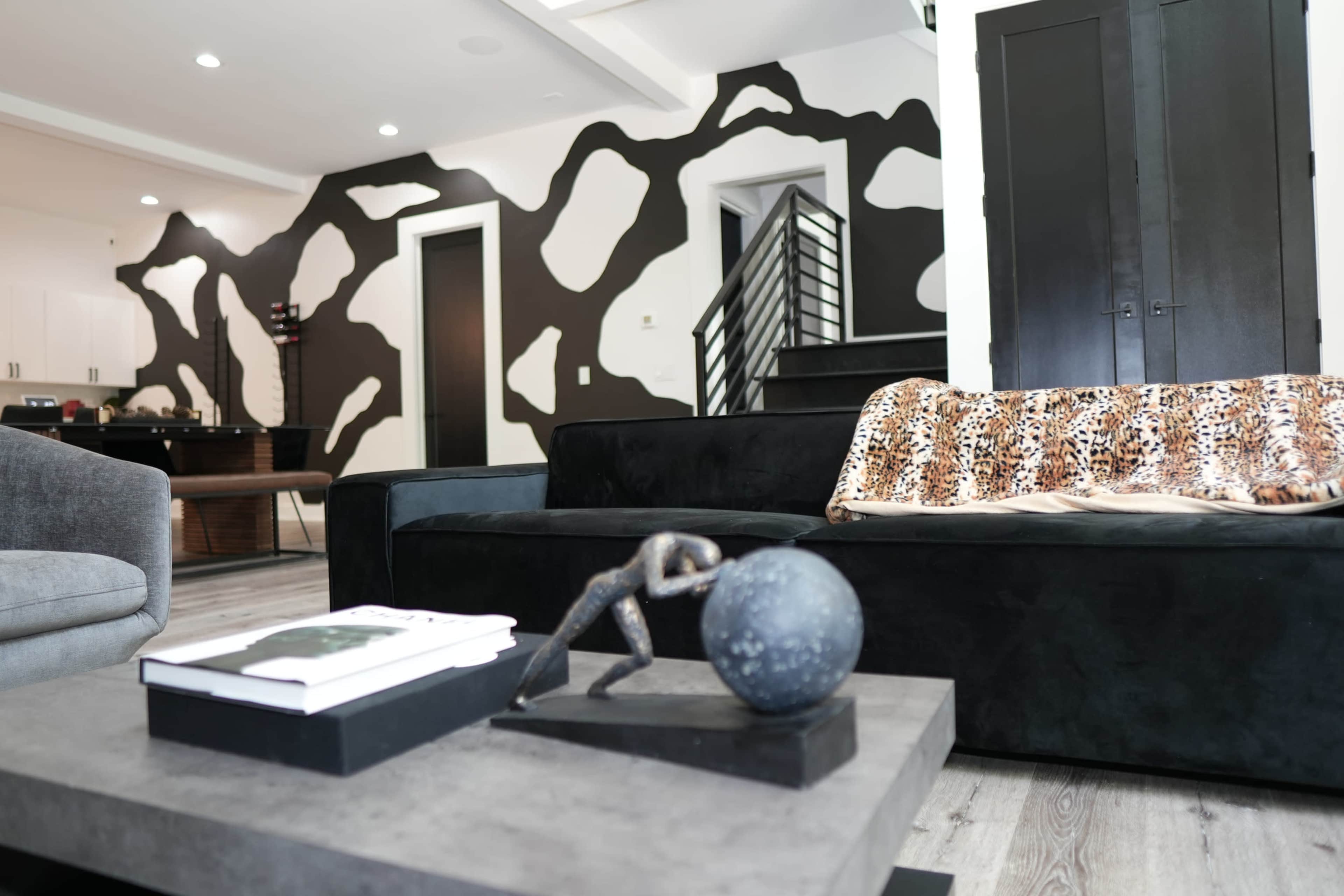 A modern living room with a black couch, a decorative coffee table featuring a sculpture, and a wall adorned with an abstract black and white pattern.
