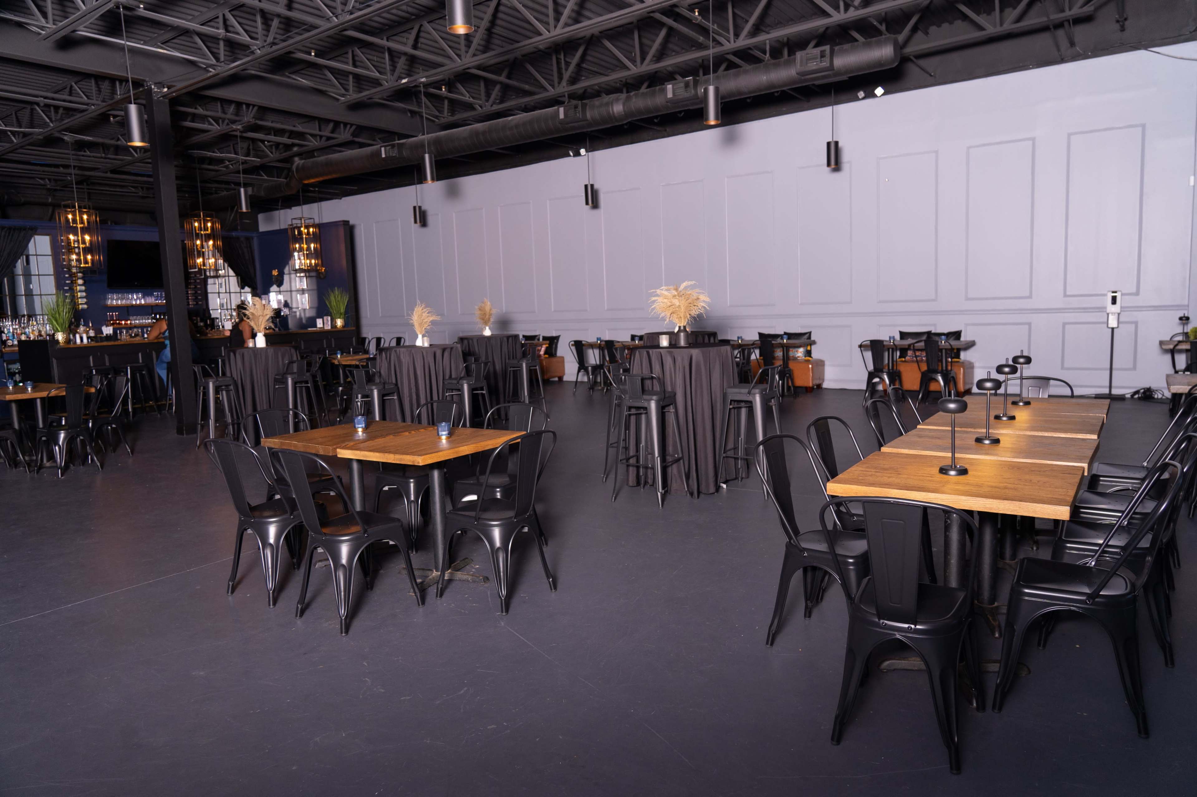 An empty event space with black tablecloths covering tall tables and wooden tables set up in a spacious, industrial-style interior.