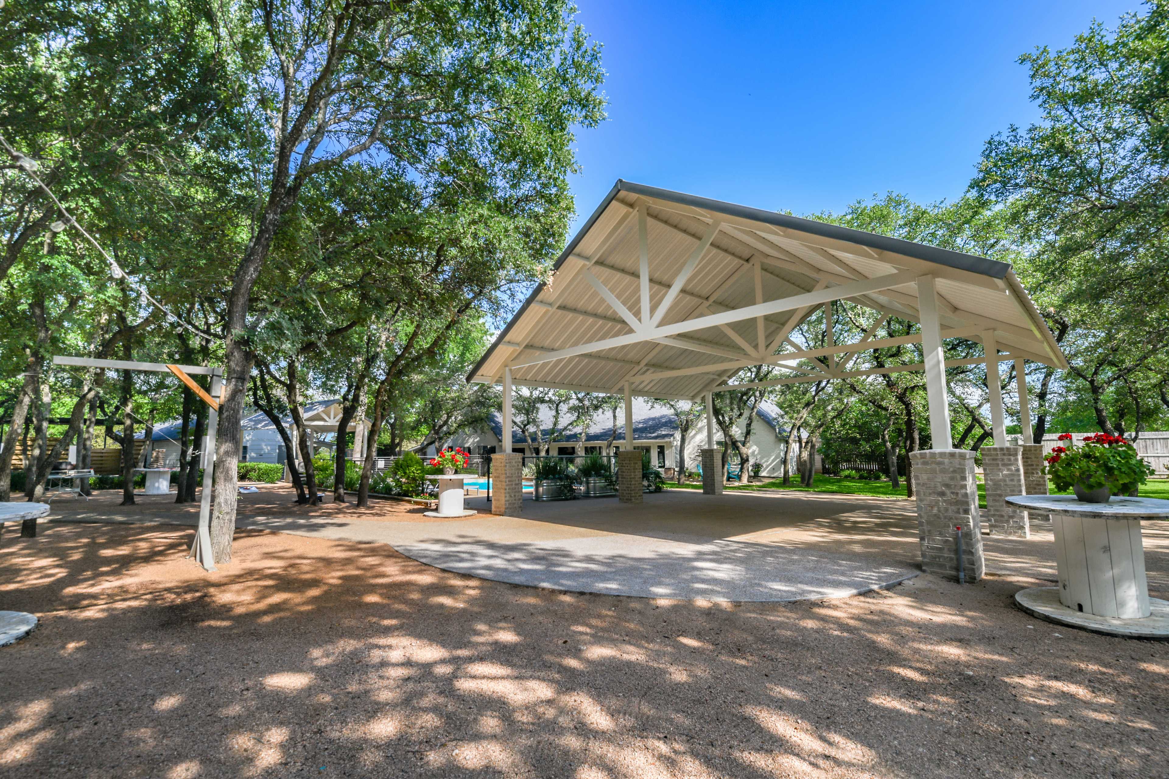 A spacious outdoor pavilion surrounded by trees and gravel paths.