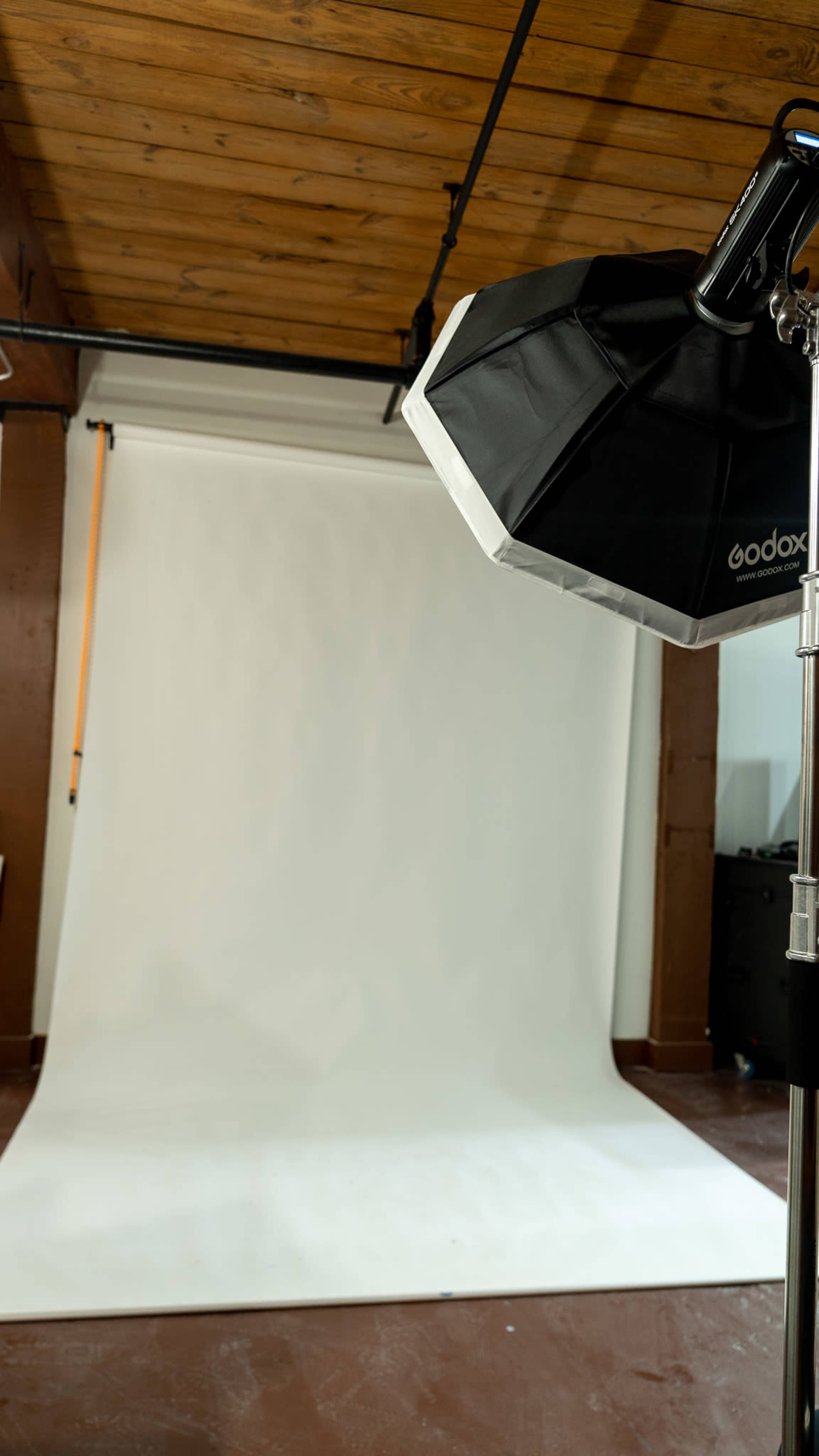 A photography studio is set up with a white backdrop and a softbox light on a stand.