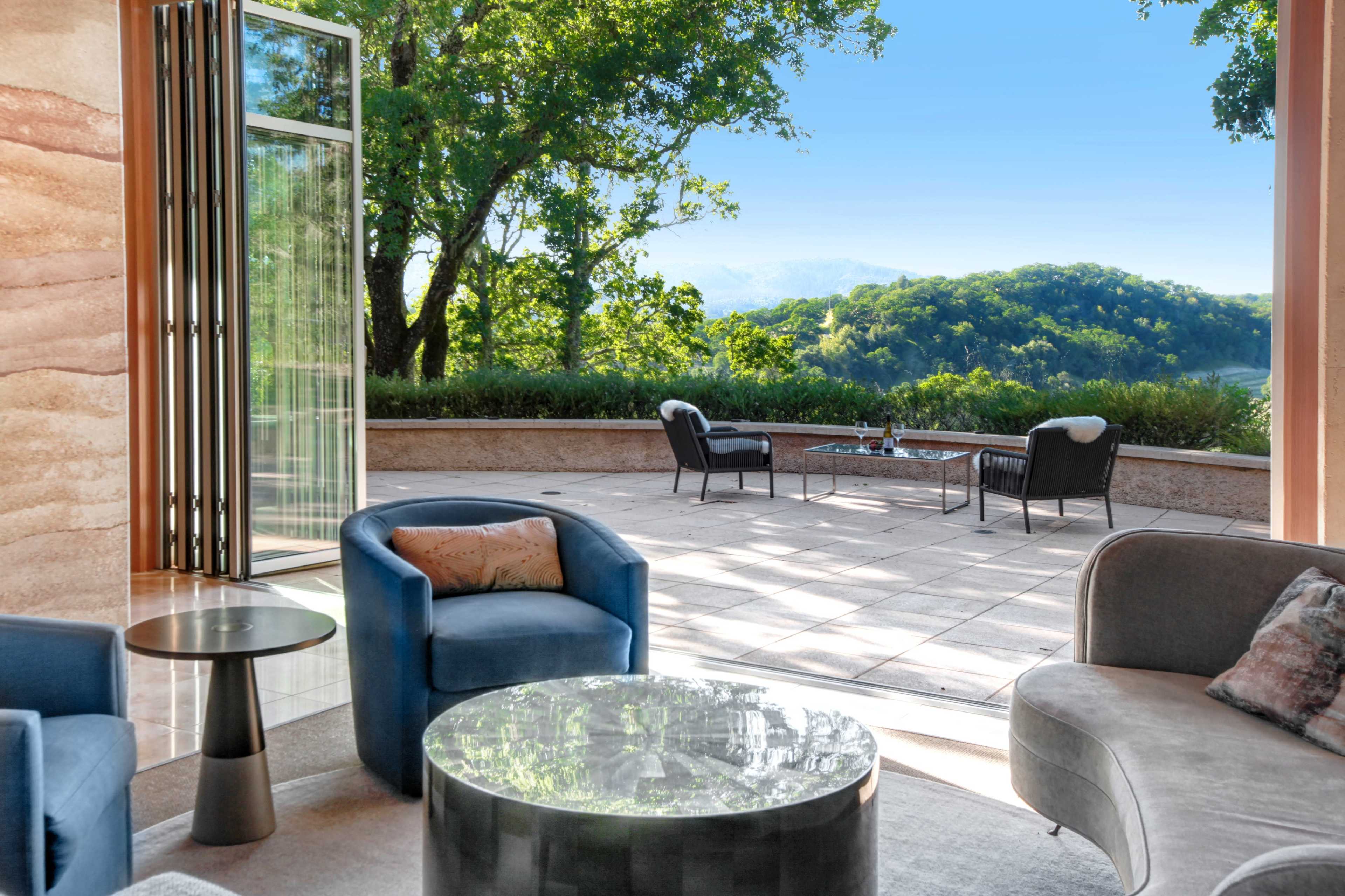 A modern outdoor patio with a view of trees and mountains, featuring a glass door and comfortable seating arrangements.