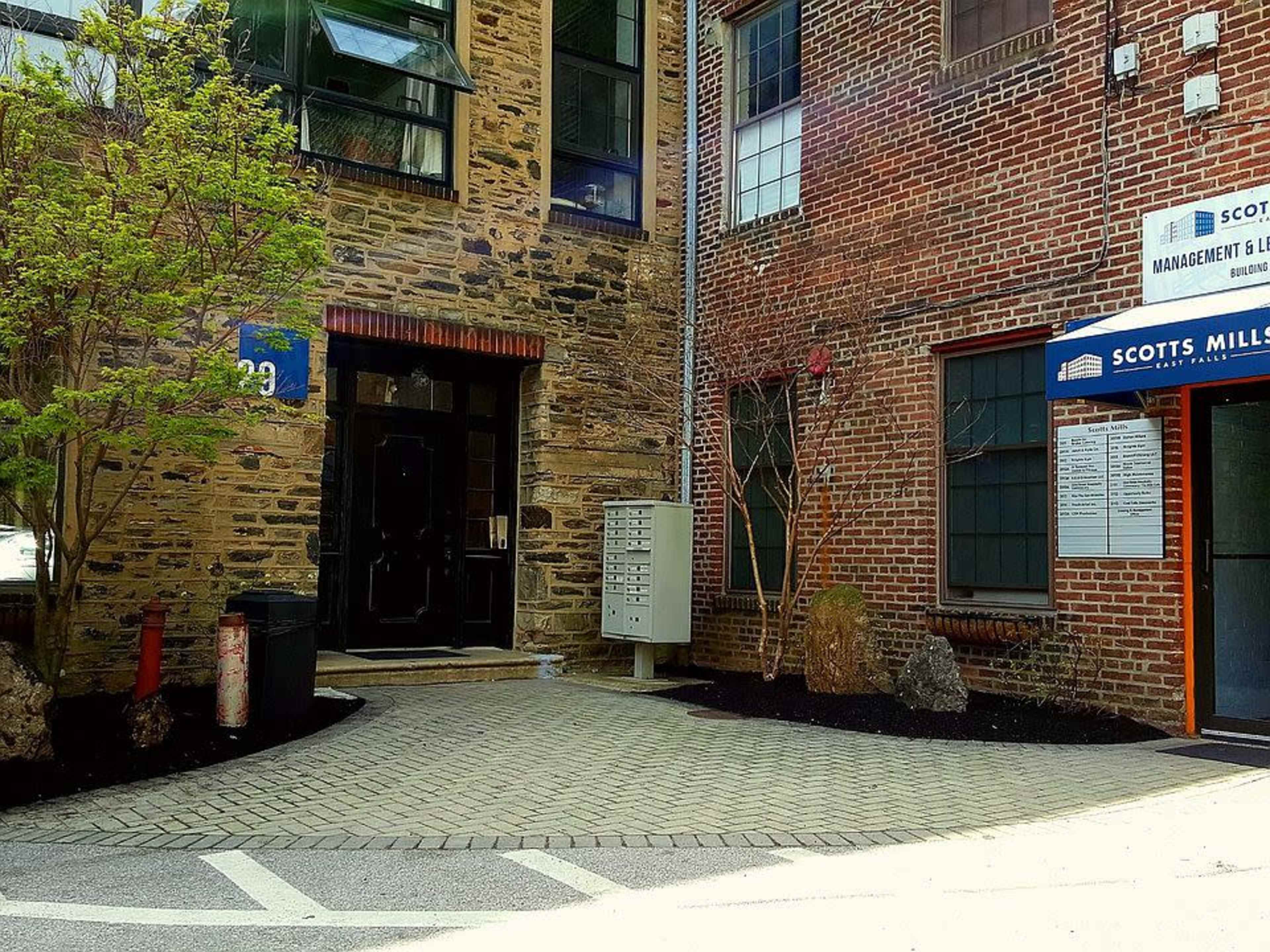 The image shows a brick building entrance with a mailbox on the side and a sign for Scott's Mill Management.