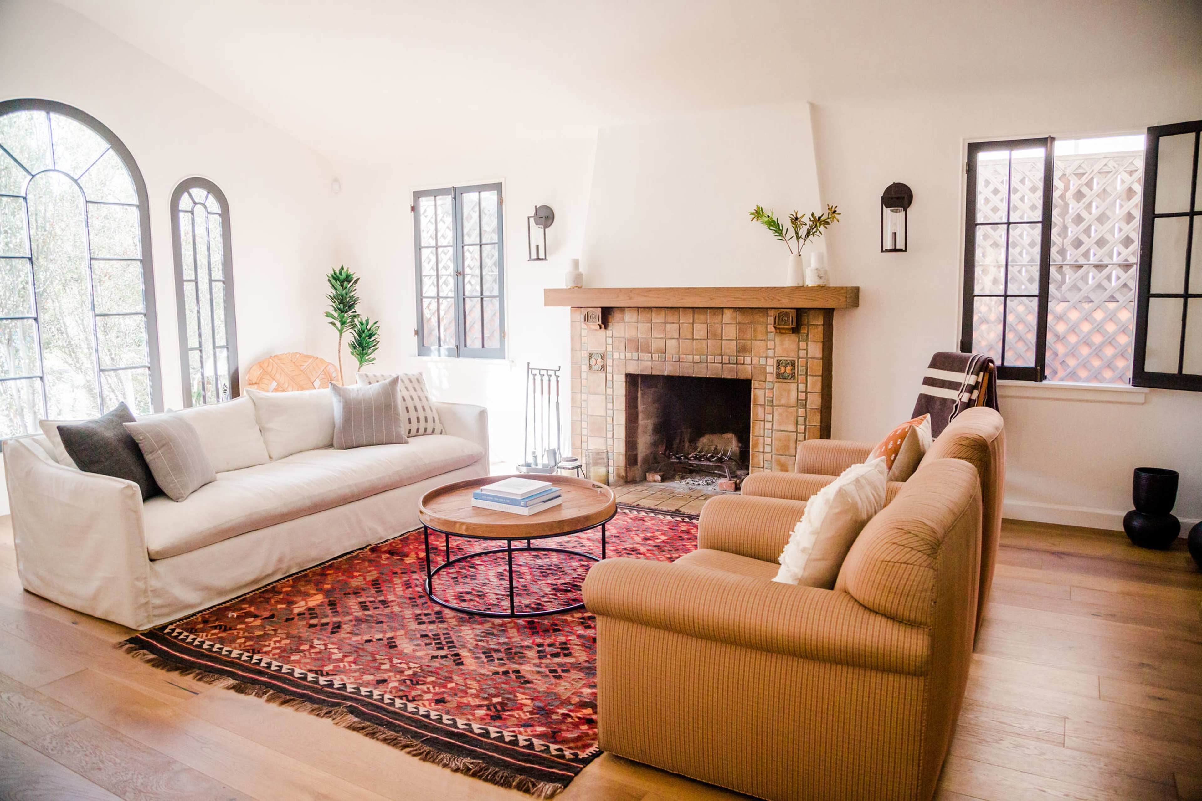 A bright living room features a white sofa, a brown couch, a round coffee table, and a fireplace with decorative tiles.