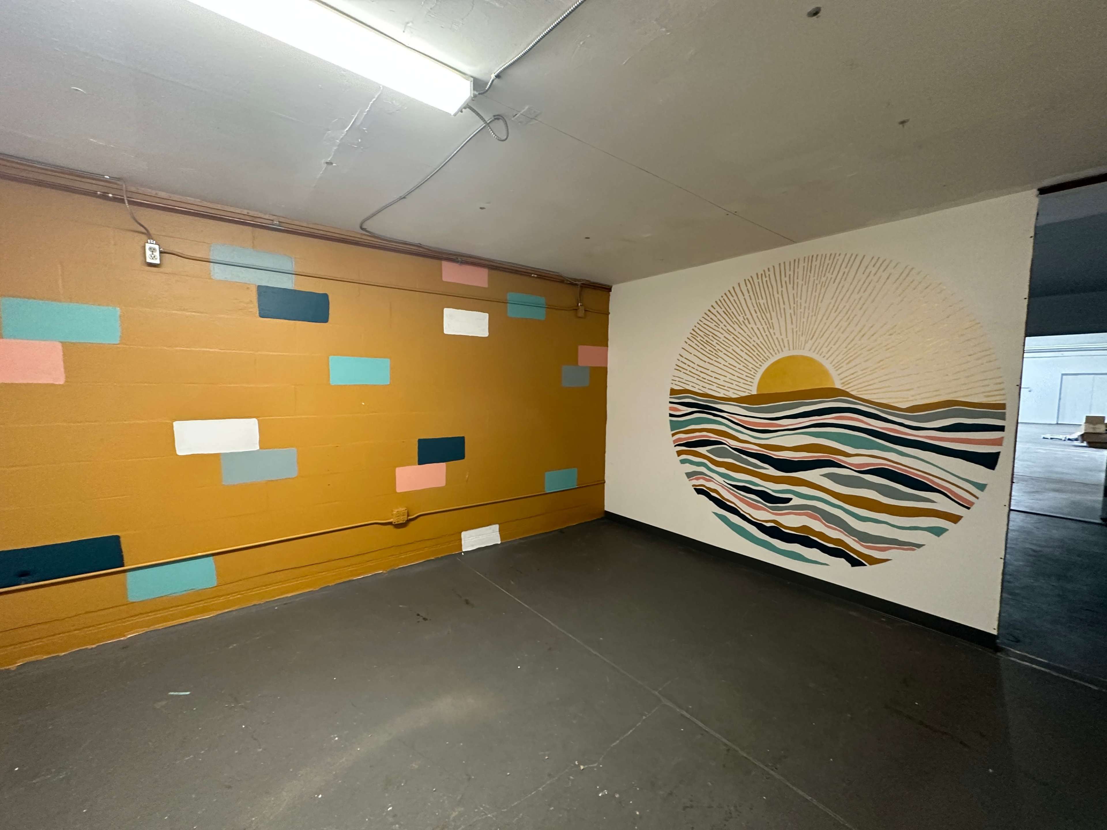 A room with a painted wall featuring a circular sun and wave design on one side and a wall with colorful rectangular shapes on the other.