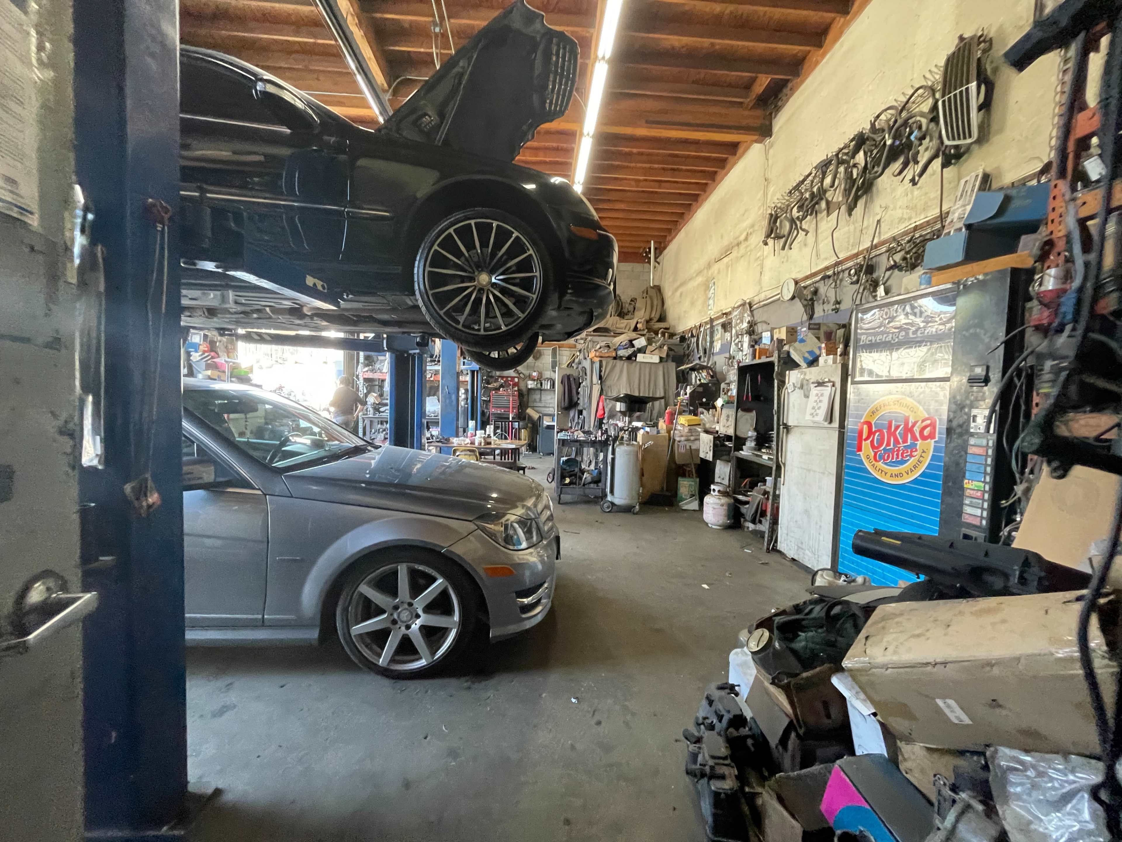 The image shows an auto repair shop with several vehicles, tools, and equipment visible, including a car on a hydraulic lift.